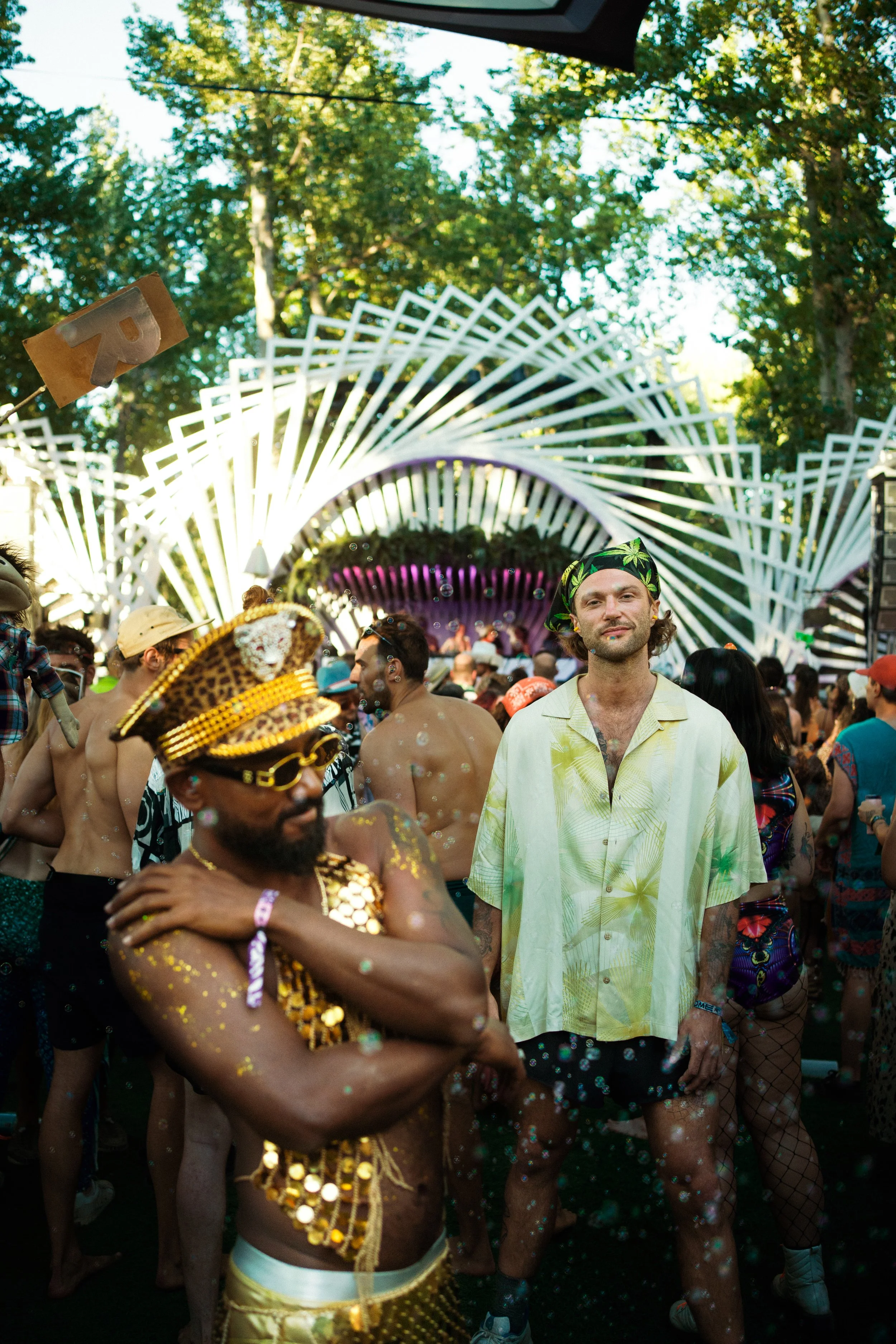 People enjoying a lively outdoor party or festival with a stage in the background, surrounded by trees, during daytime. Some participants are dressing in colorful, festive clothing. ; 10 Things I Learned Rawdogging a 4-Day Rave Without Booze or Drugs