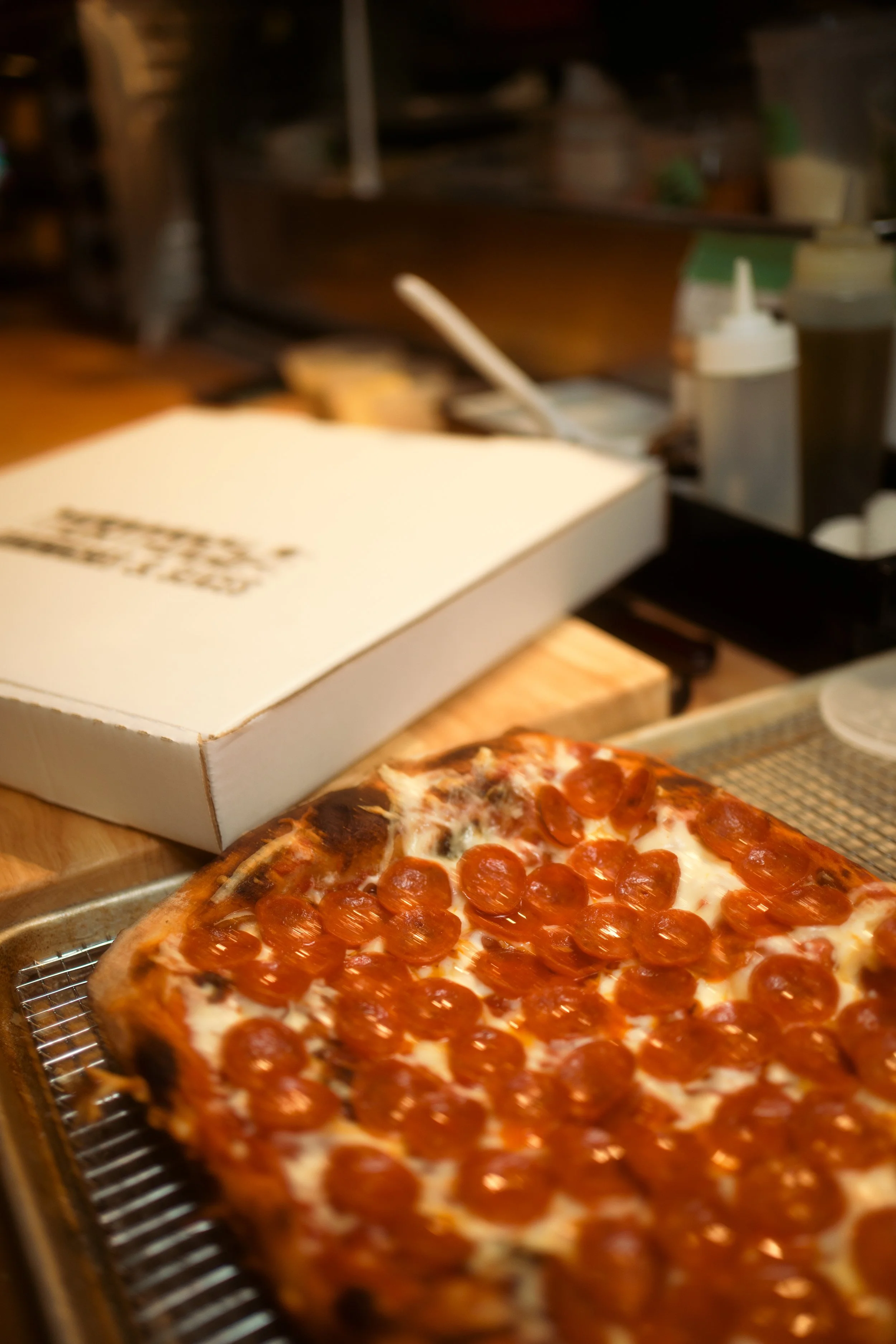 A box of pizza sits on a wire rack in a kitchen or pizzeria setting.