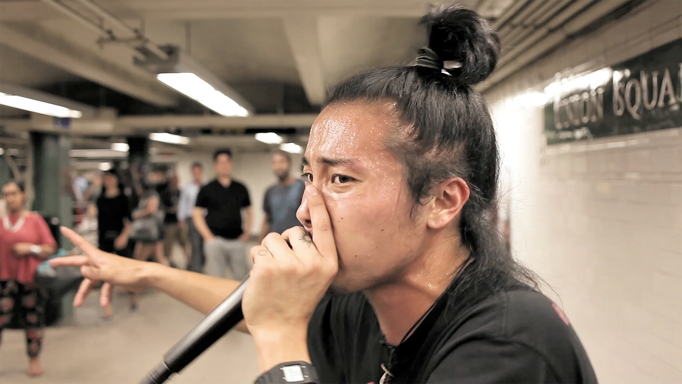 Street performer singing into a microphone with a crowd of people in the background at a subway station.