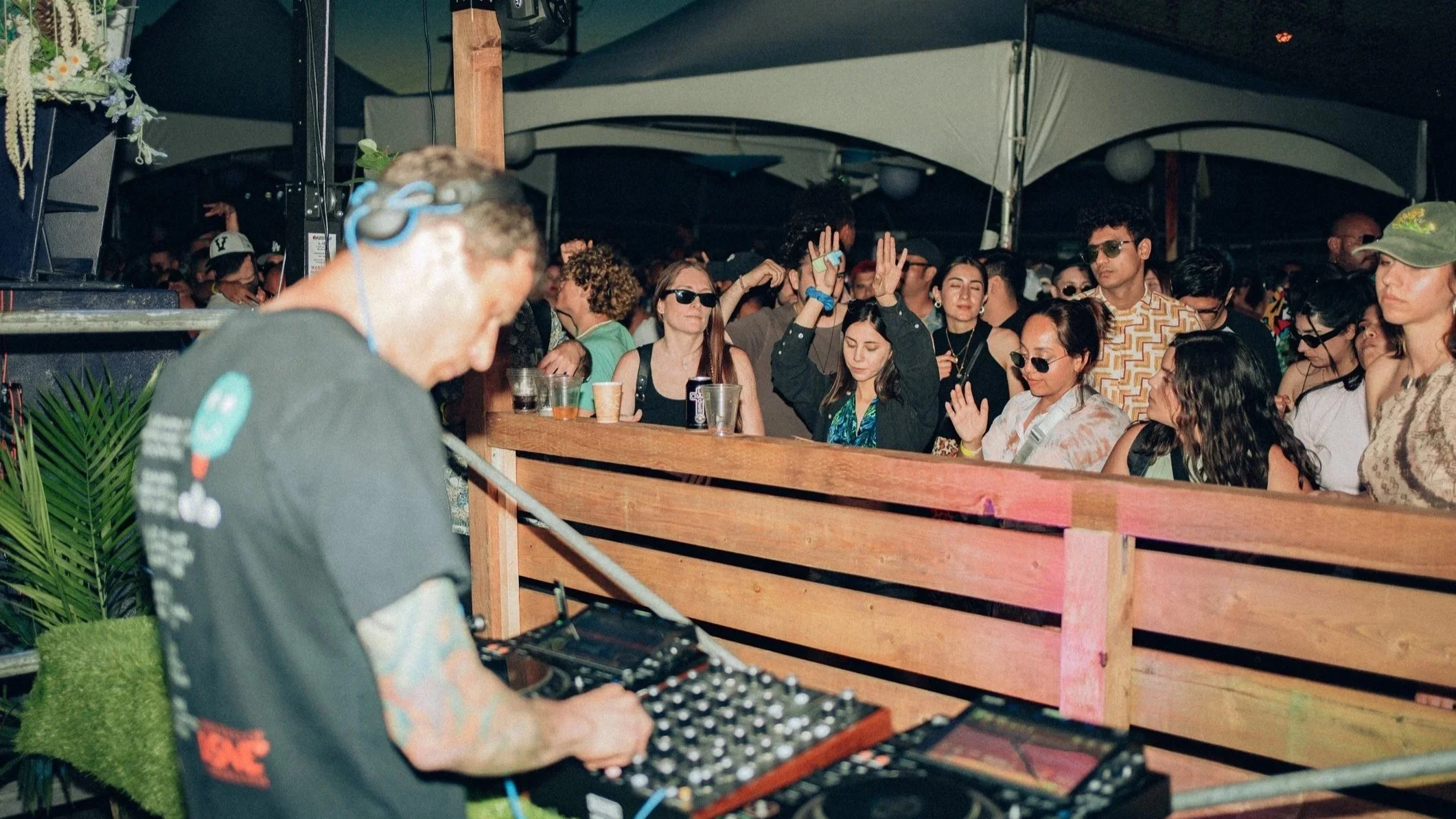 A DJ performs at an outdoor music event as a crowd of people dance and enjoy the night.