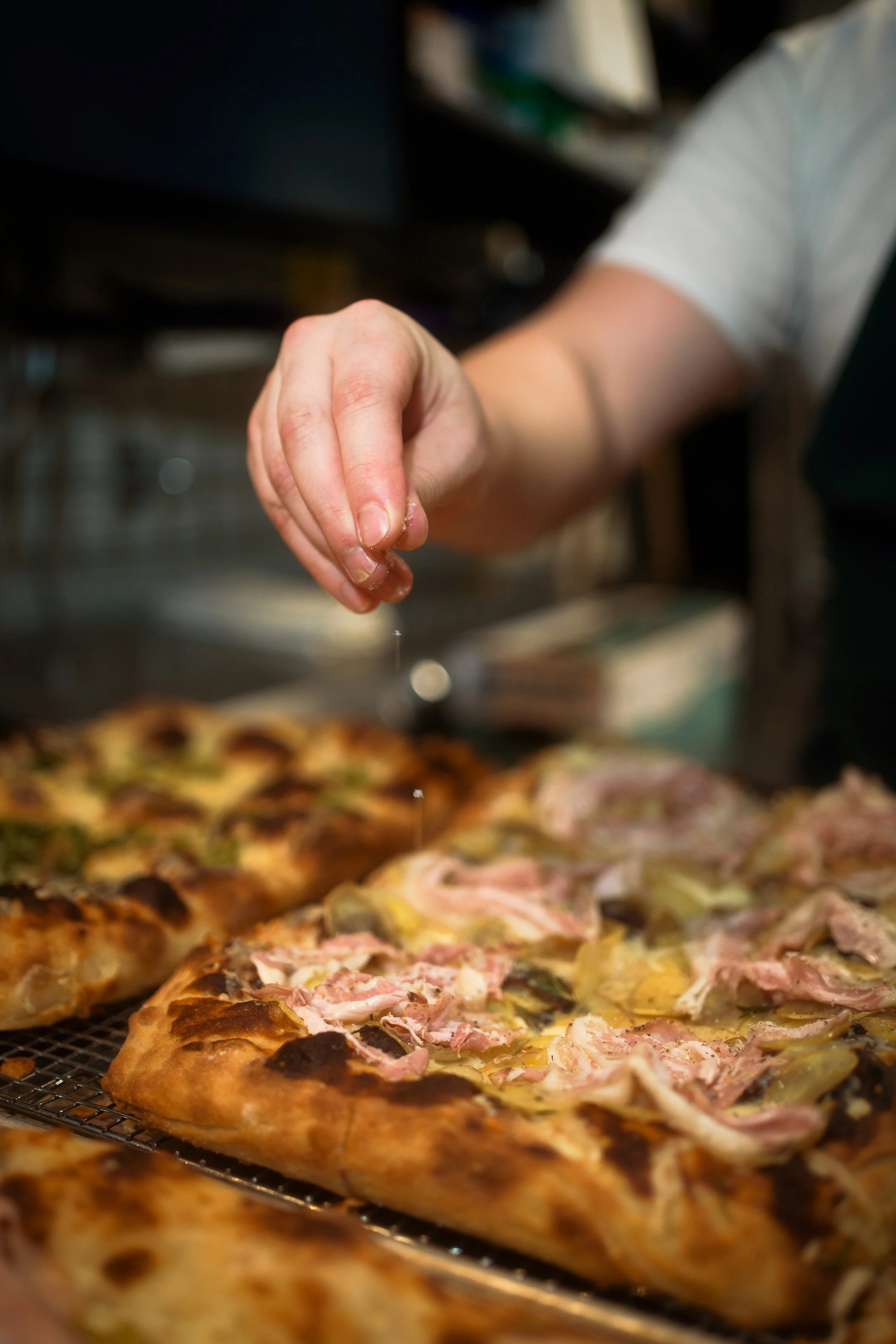 Close-up of a person sprinkling salt on a freshly baked pizza topped with ham, artichokes, and cheese.
