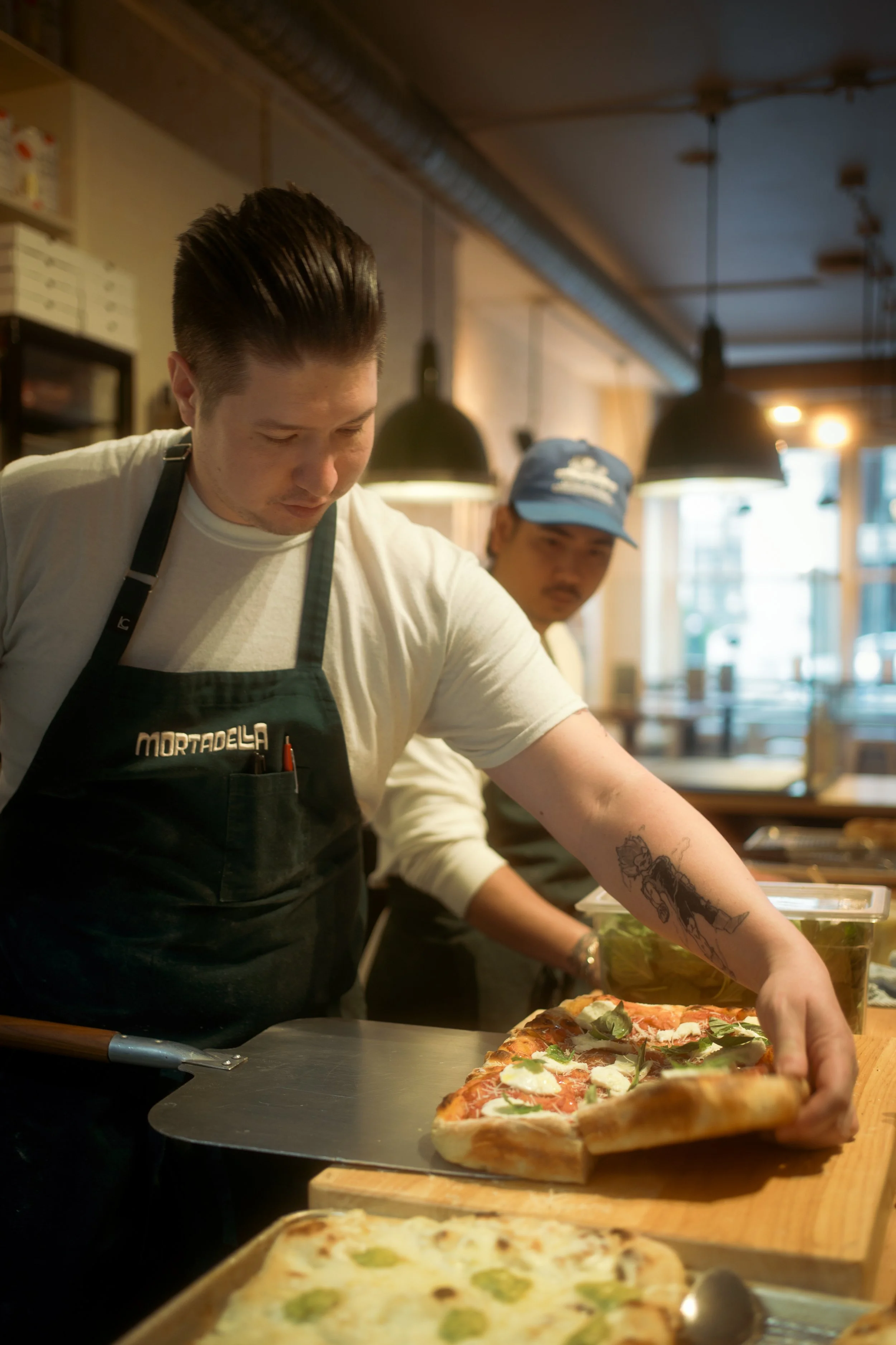 Two pizza chefs preparing pizza in a restaurant kitchen.