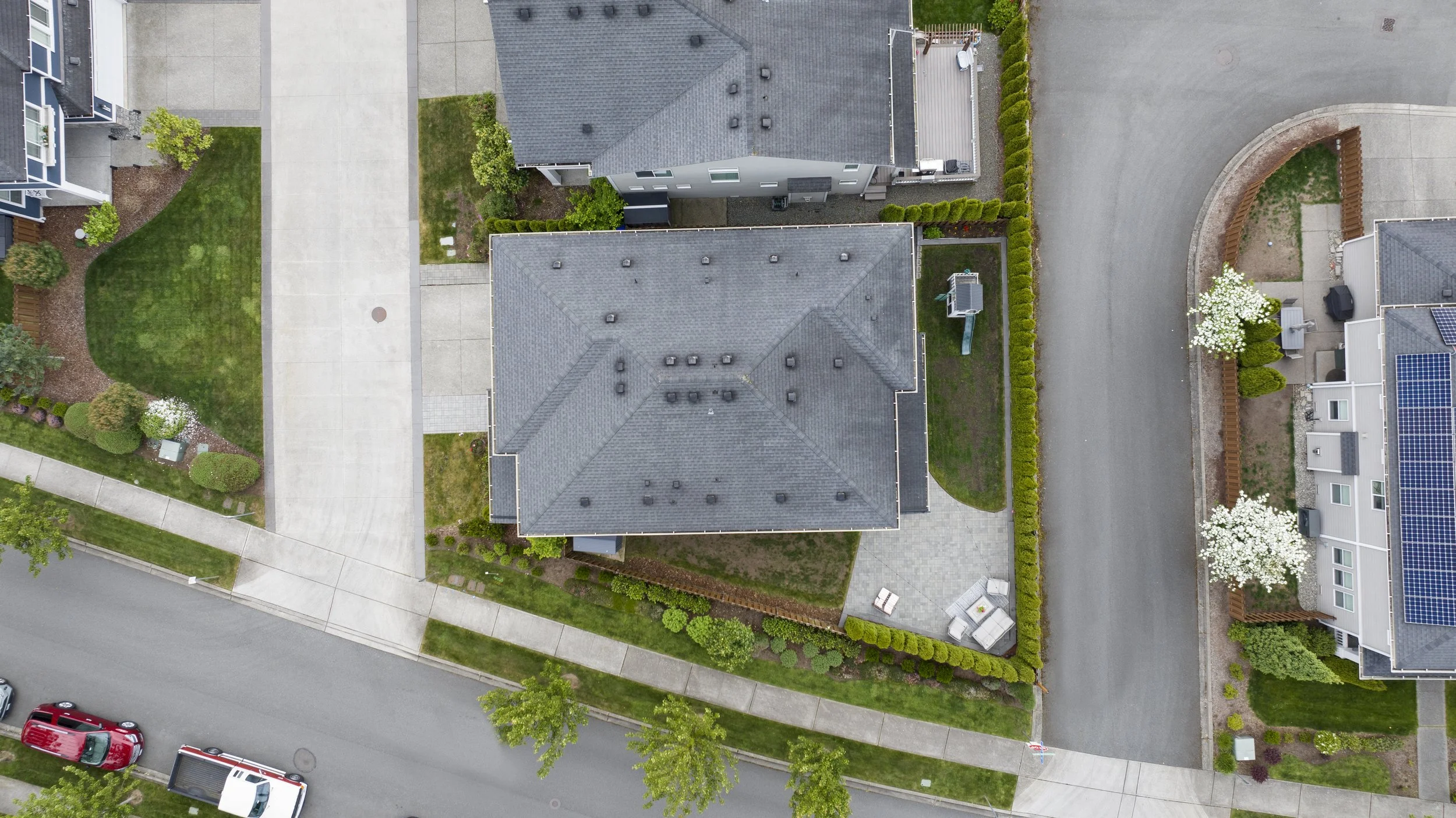 Aerial view of a residential neighborhood showing houses, manicured lawns, driveways, and parked cars along a curved street.