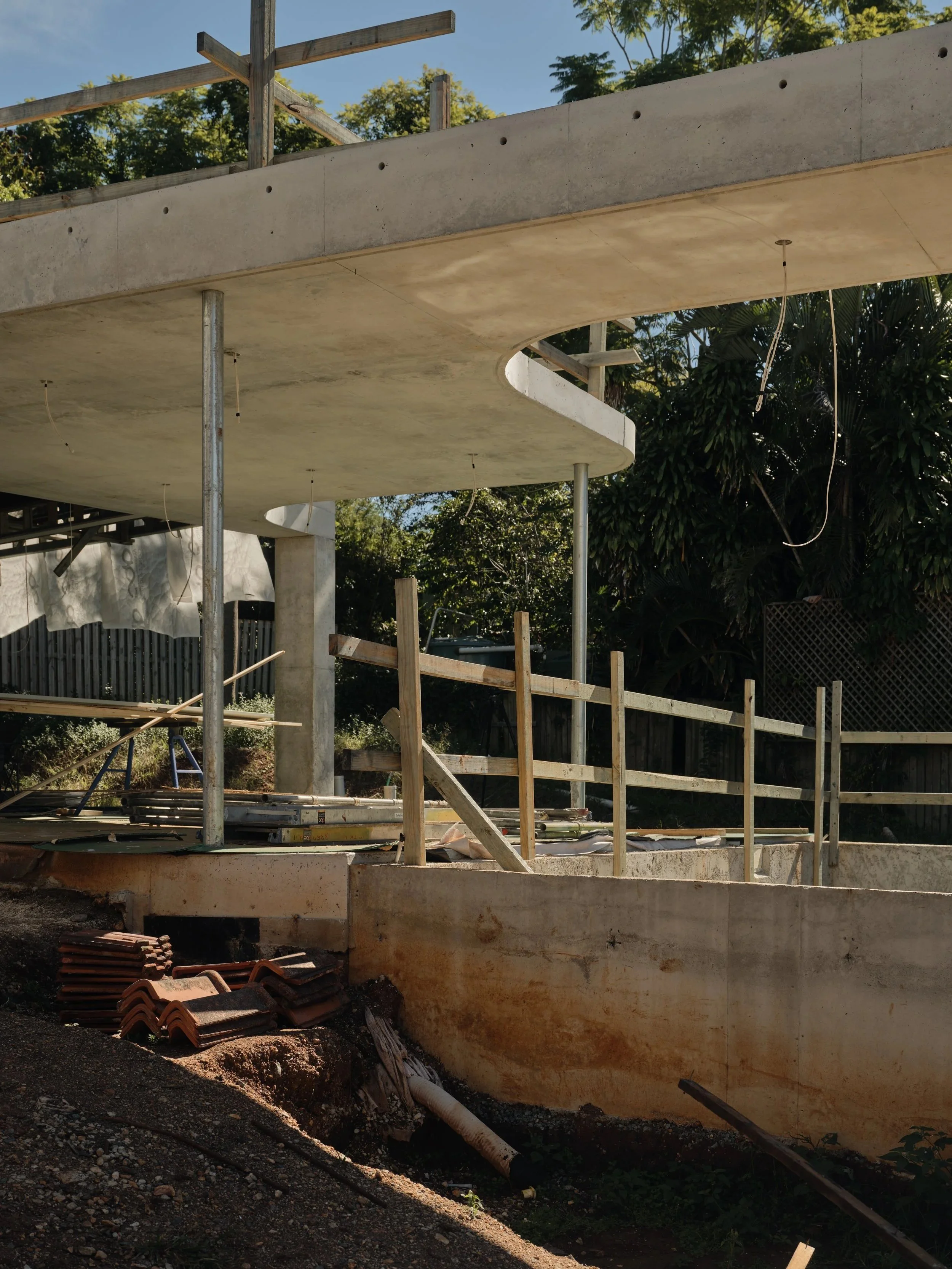 Curved concrete slab and structural supports during mid‑construction, showing formwork, roof tile staging and site preparation for a major architectural renovation by Allen Brothers Construction.
