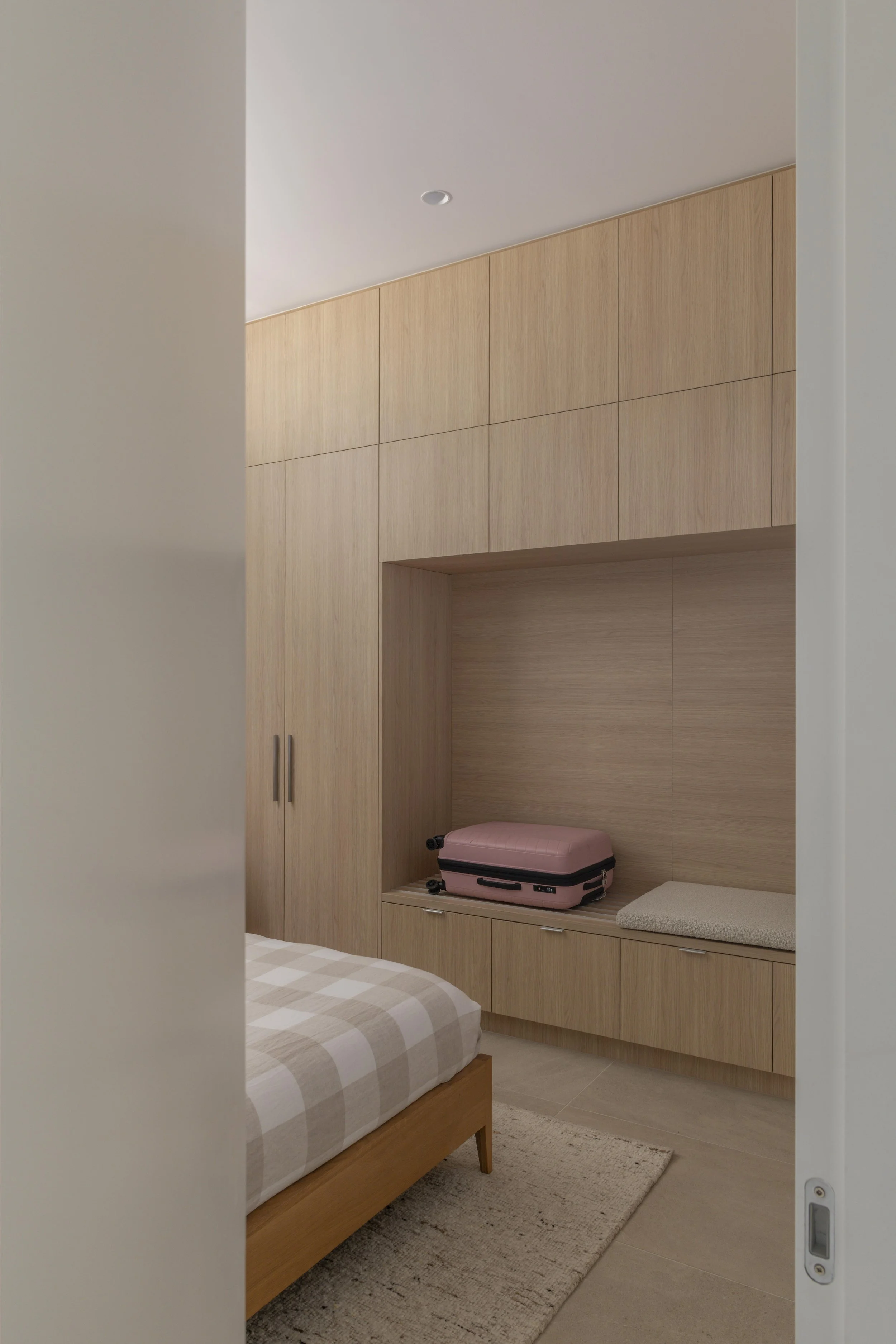 This minimalist bedroom at Project124 features bespoke timber joinery with integrated storage, a recessed seating nook, and a warm, neutral palette that enhances the calm, functional design. The refined detailing, natural textures, and thoughtful lay
