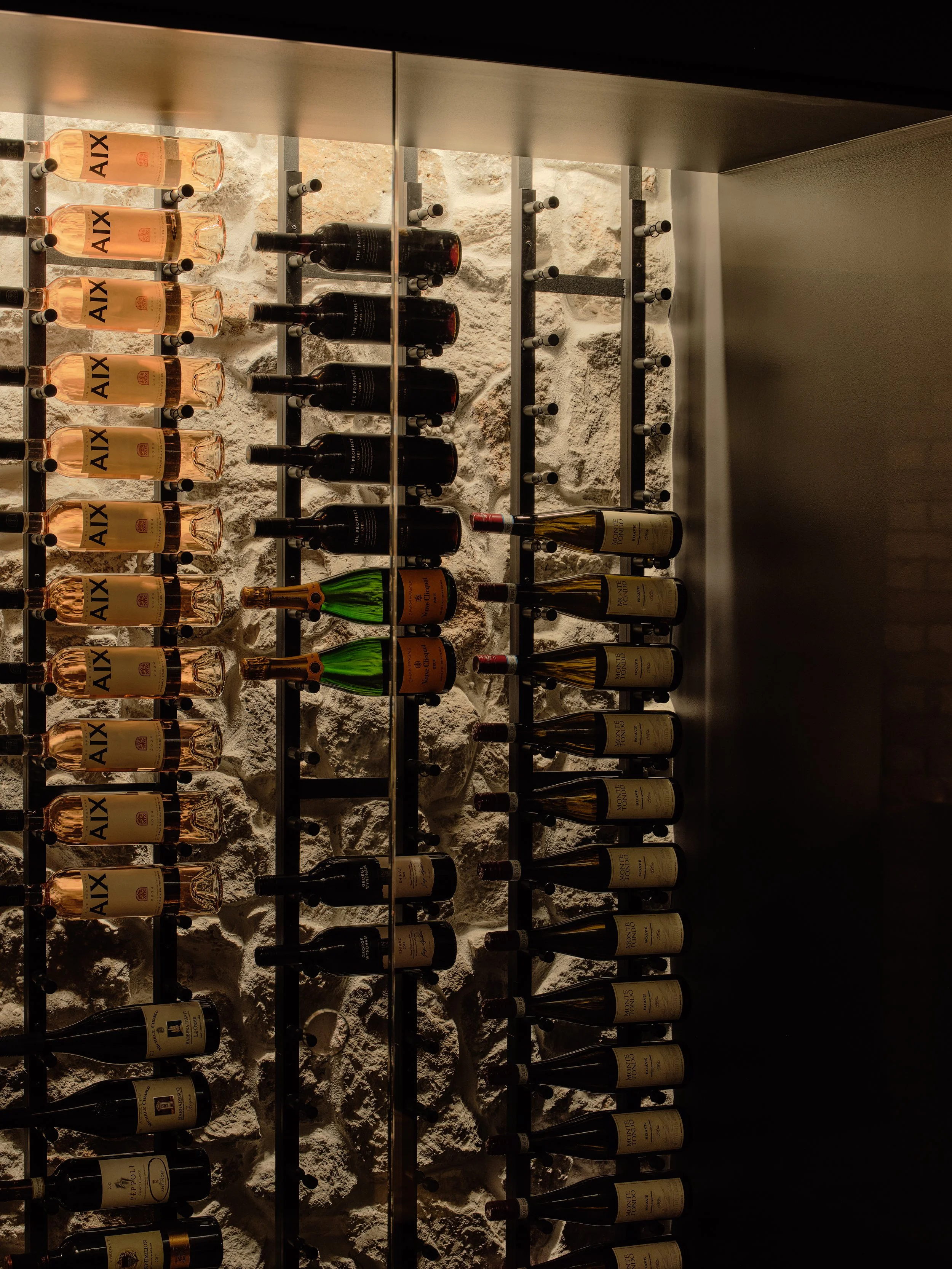 Wine room display wall with stone backdrop and illuminated bottle racks