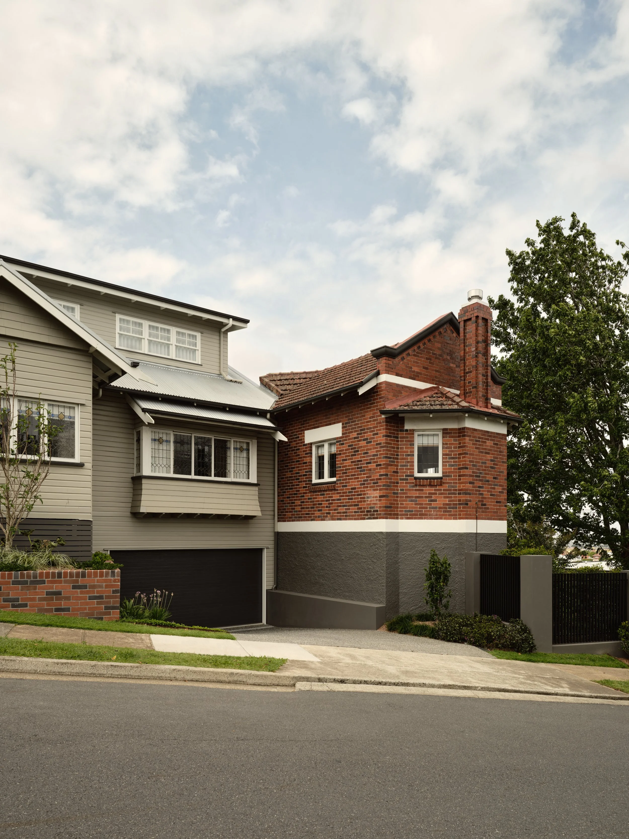 Renovated heritage home with modern cladding and garage on a sloping site beside a red‑brick character house