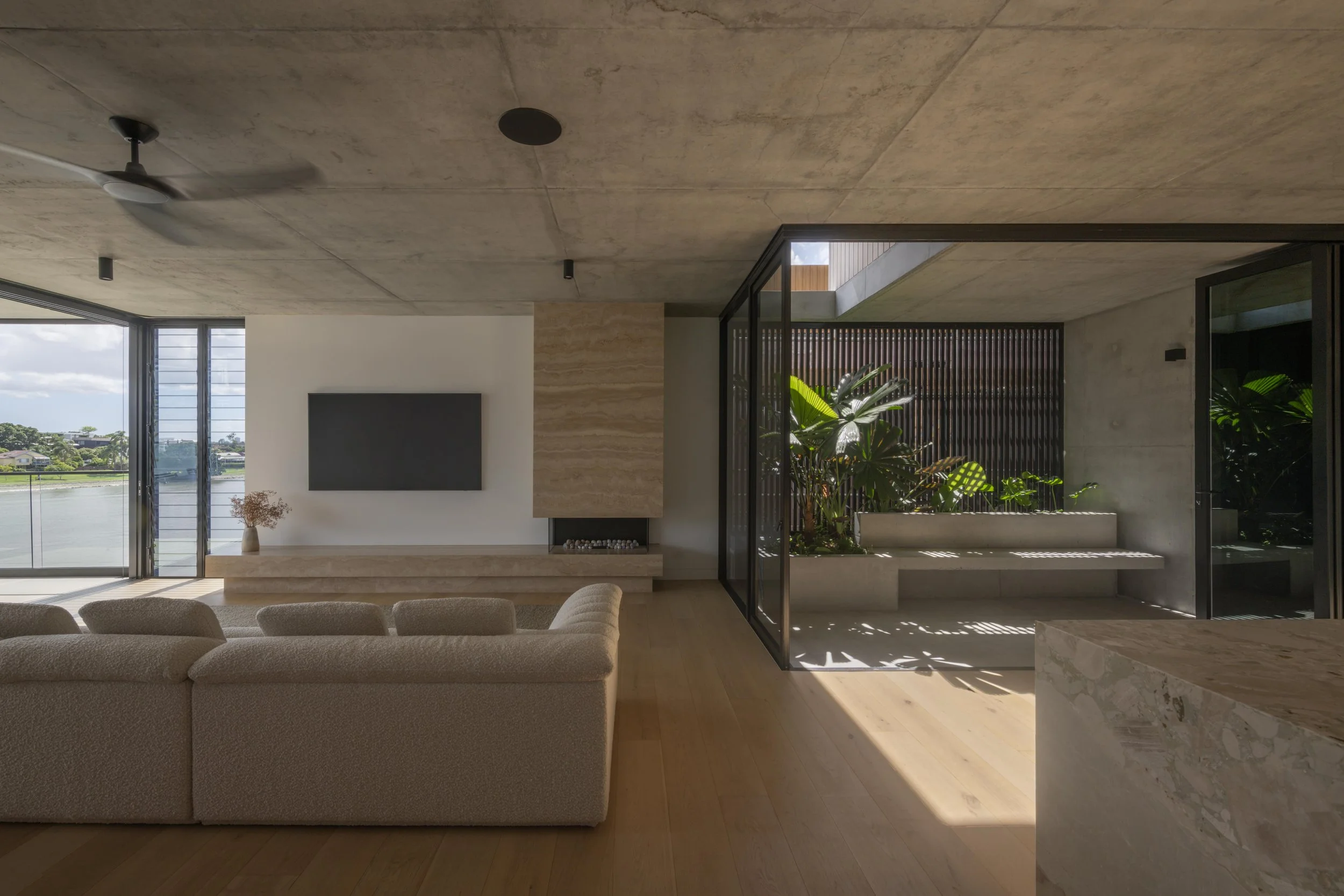 Minimalist living room with travertine fireplace, indoor garden, and river views in a luxury Brisbane home by Allen Brothers Construction.