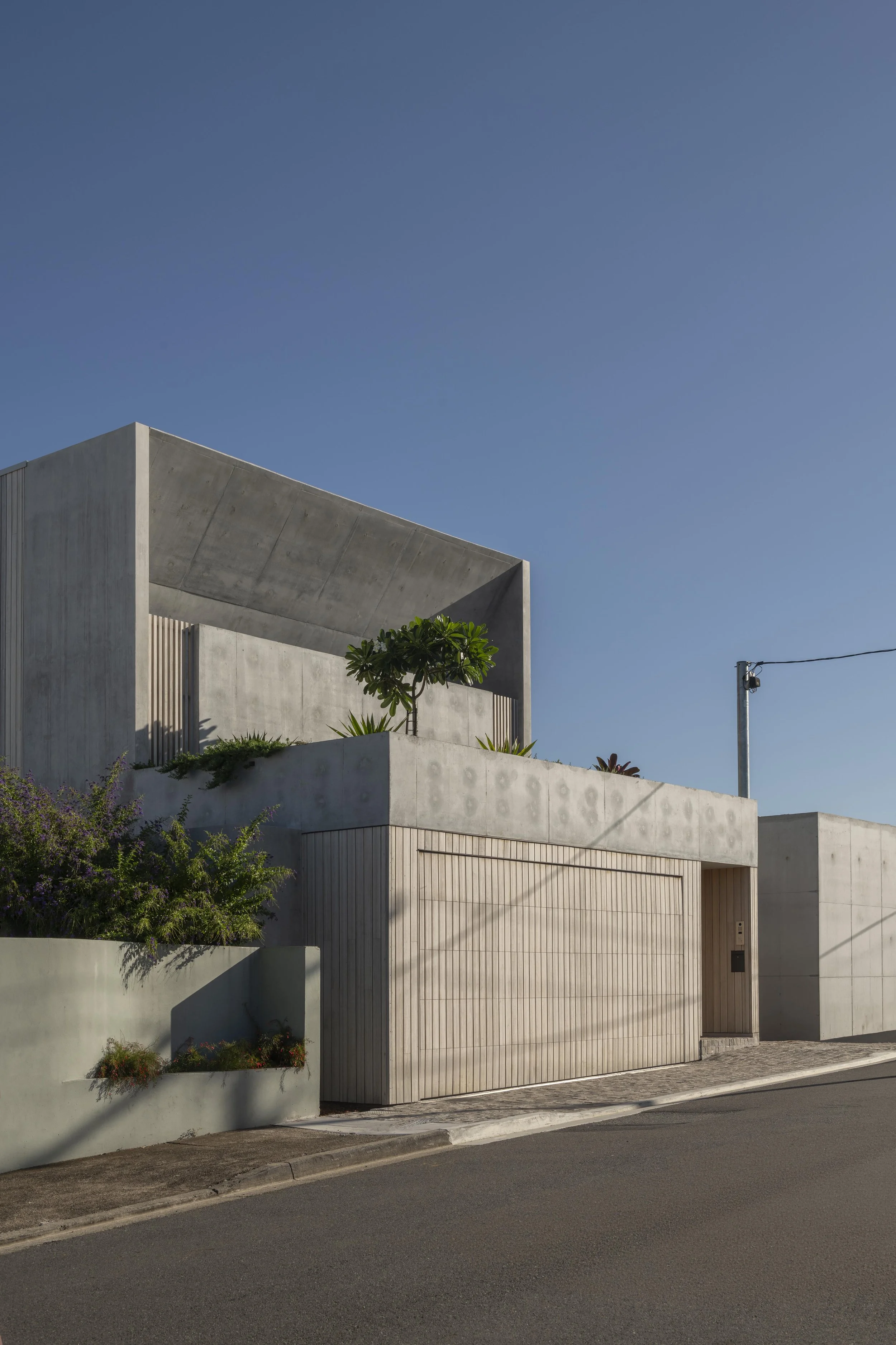 Modern riverfront home façade with off‑form concrete, timber cladding, and rooftop garden by Allen Brothers Construction