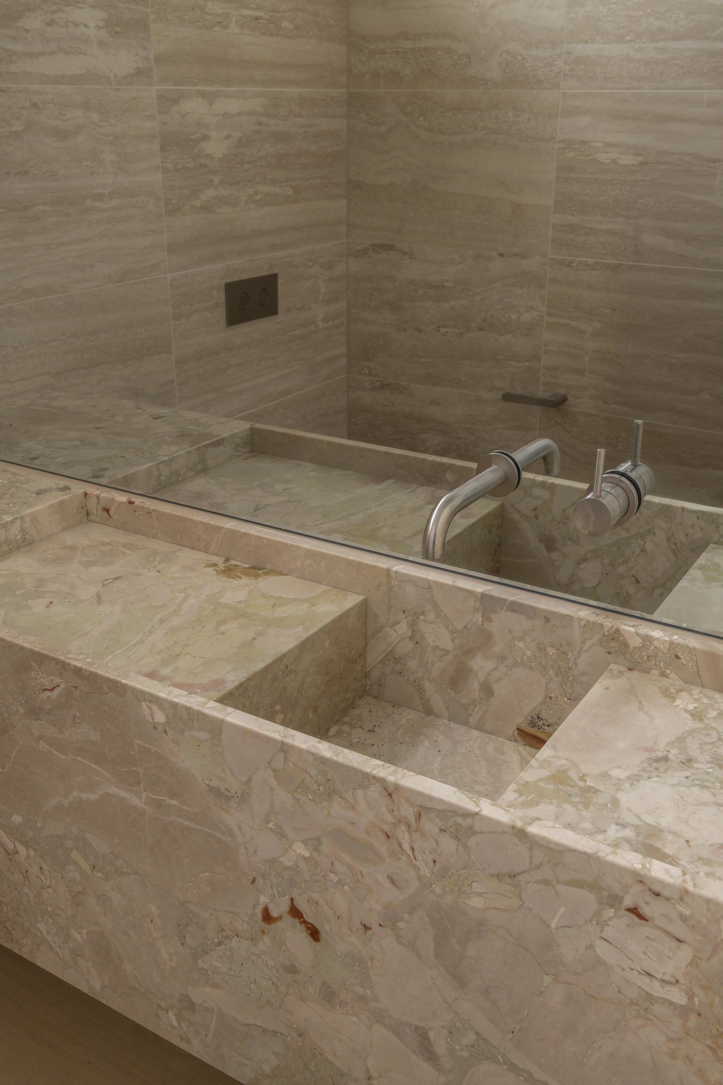 This refined vanity detail at Project124 features a sculpted stone basin, wall‑mounted tapware, and a seamless continuation of natural stone across the benchtop and splashback. The minimalist composition, warm tonal palette, and precise detailing hig