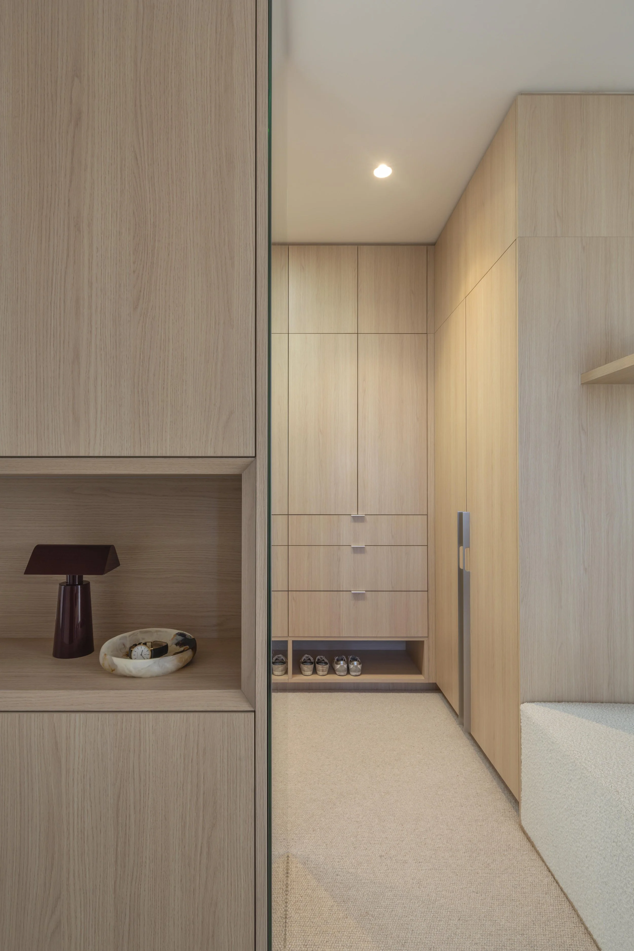 This refined walk‑in corridor at Project124 features warm timber cabinetry, integrated shelving, and soft, ambient lighting that highlights the minimalist detailing. A curated display niche introduces subtle styling, while the recessed shoe shelf and