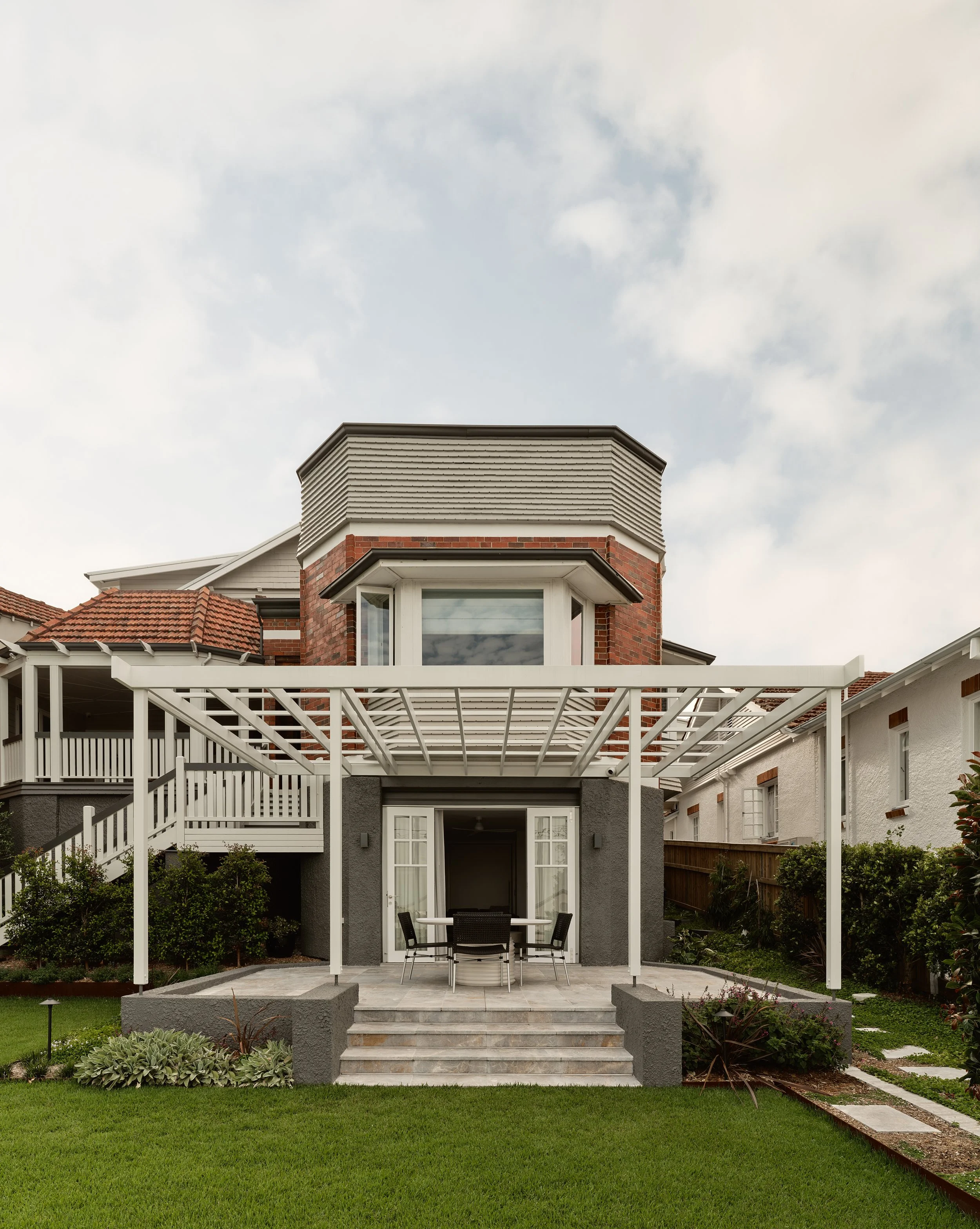 Rear view of renovated heritage home with covered patio, French doors and landscaped lawn.