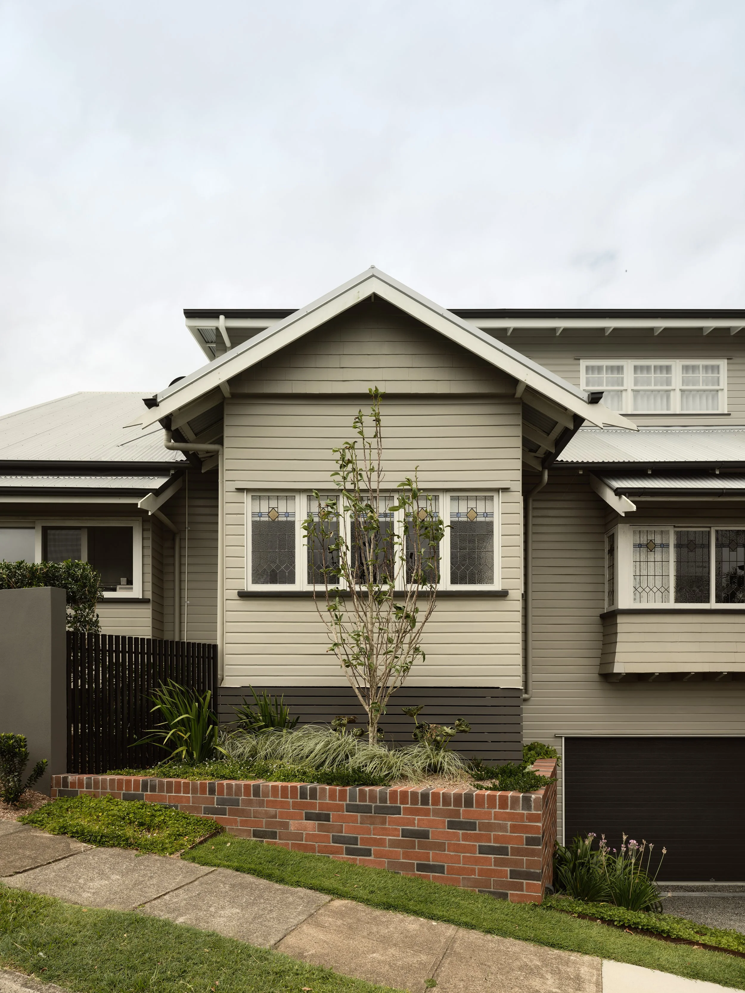 Heritage home on a sloping site with brick retaining wall, stained‑glass windows and landscaped front garden