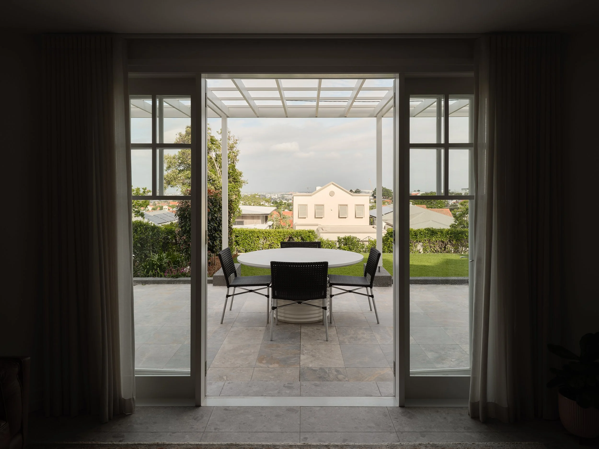 View from interior to covered patio with outdoor dining and landscaped lawn