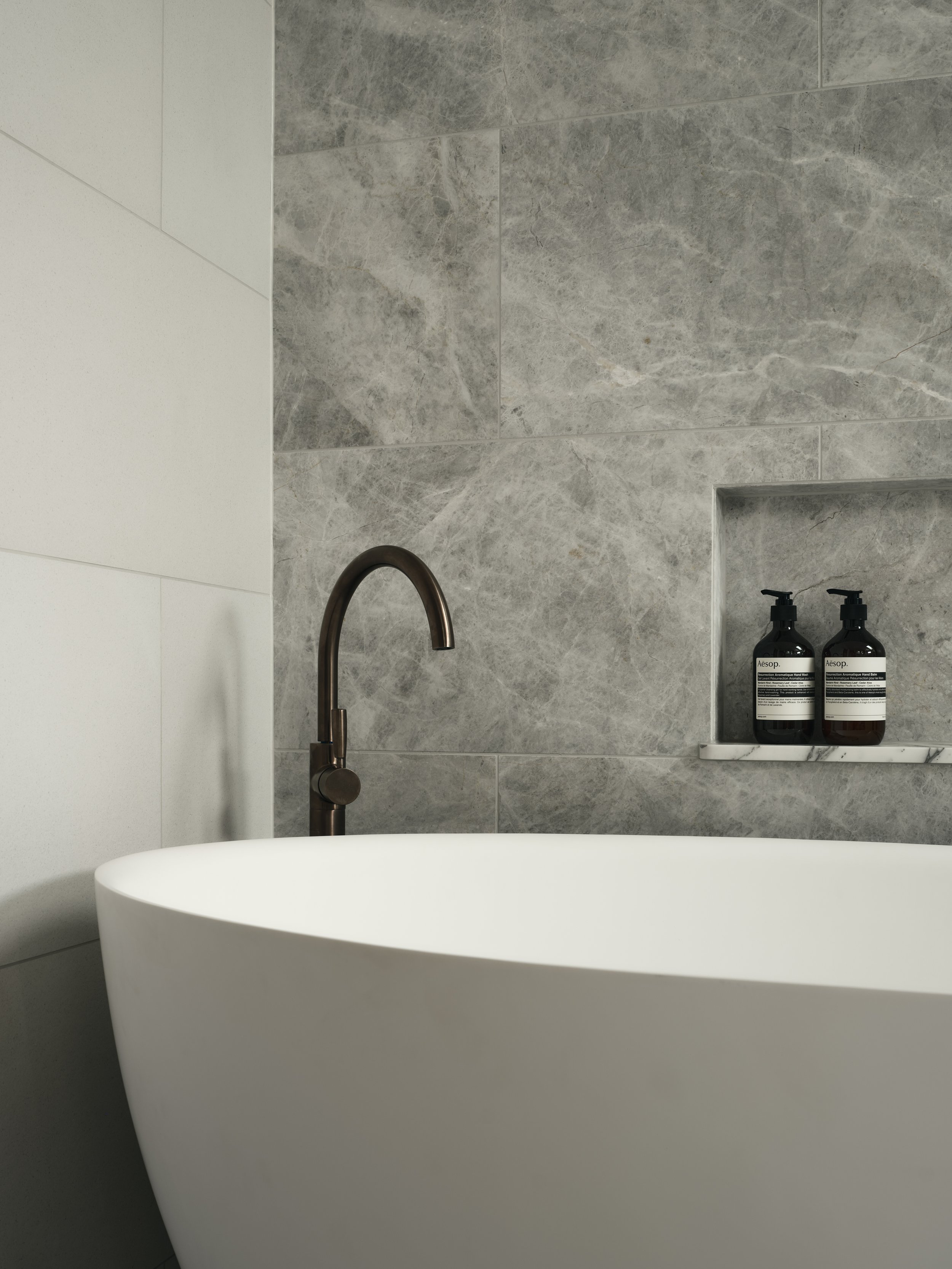 Freestanding bath with Brodware Statue Bronze tapware and marble feature wall in a luxury bathroom.