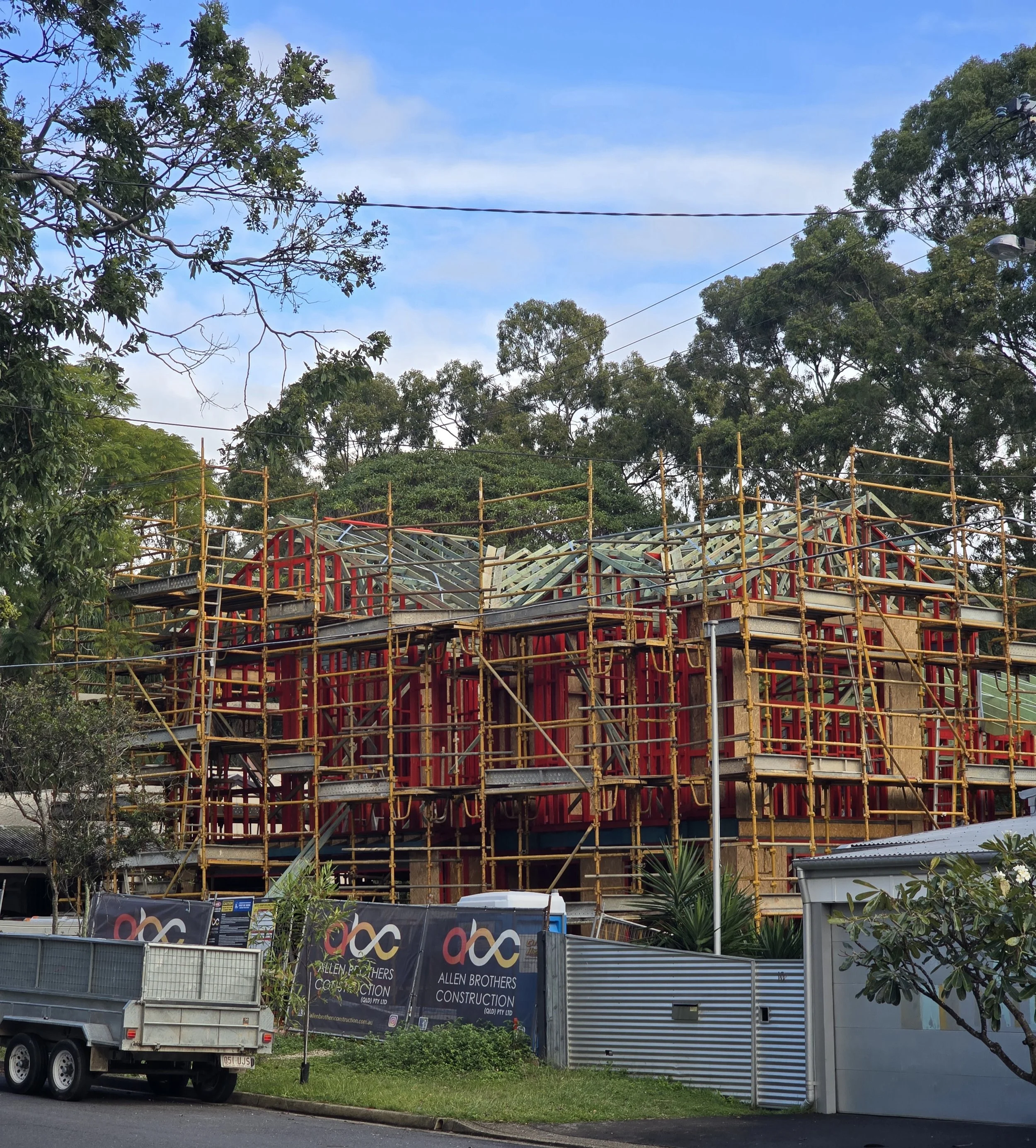 The image shows the Project 135 home during construction, fully scaffolded with the timber framing complete and roof trusses installed. The external walls are wrapped in ProClima WRB, and sections of Linea weatherboard cladding have begun. Allen Brot