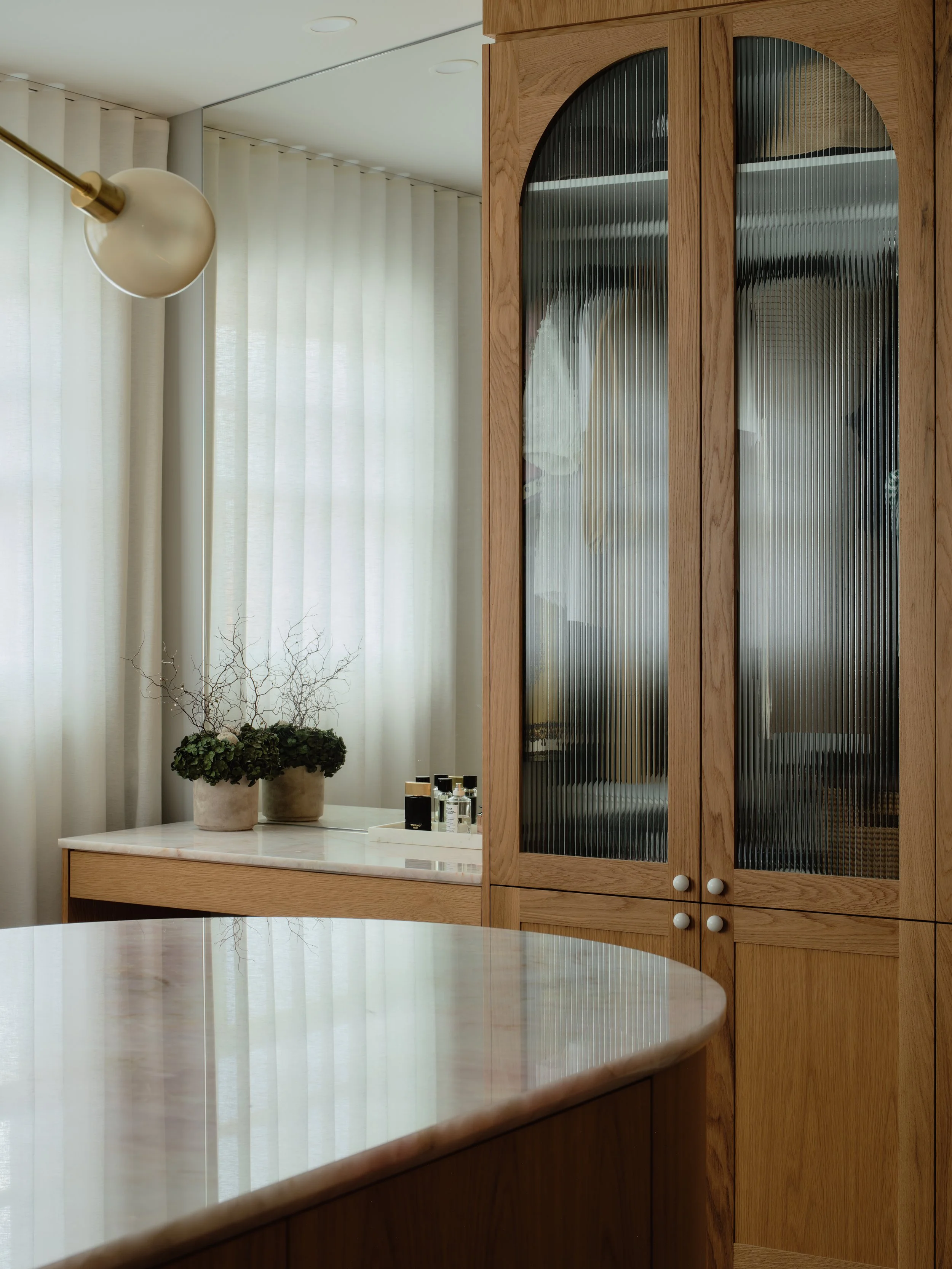 Luxury ‘her’ walk‑in robe with ribbed‑glass cabinetry, marble island and soft natural light