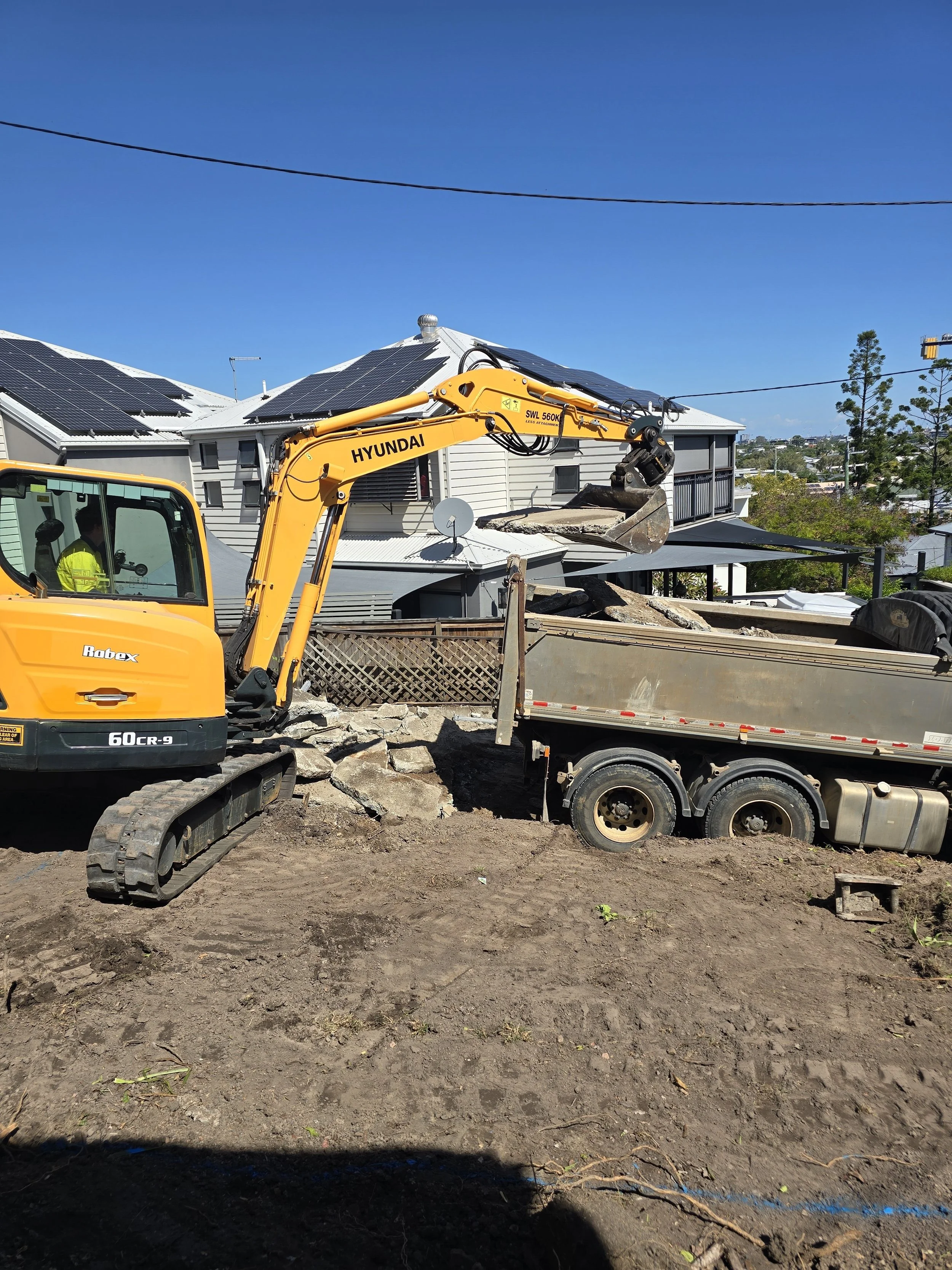 Heavy machinery removing demolition material as part of excavation and ground preparation for Bulimba house raise and build‑under project.
