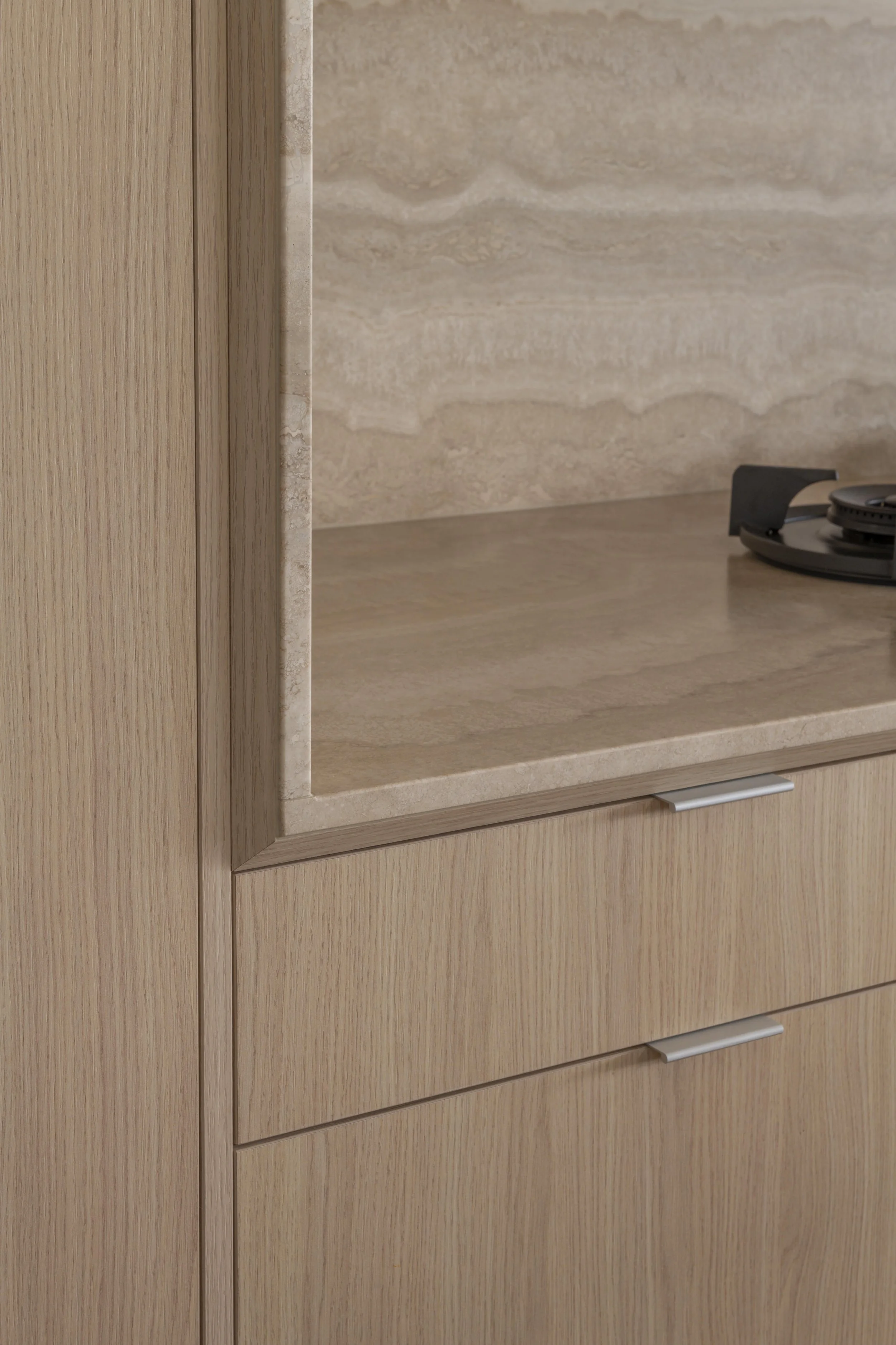 This detailed kitchen moment at Project124 highlights the warm timber cabinetry, sleek linear hardware, and layered natural stone benchtop and splashback. The rich veining and textured finish of the stone contrast subtly with the clean joinery lines,