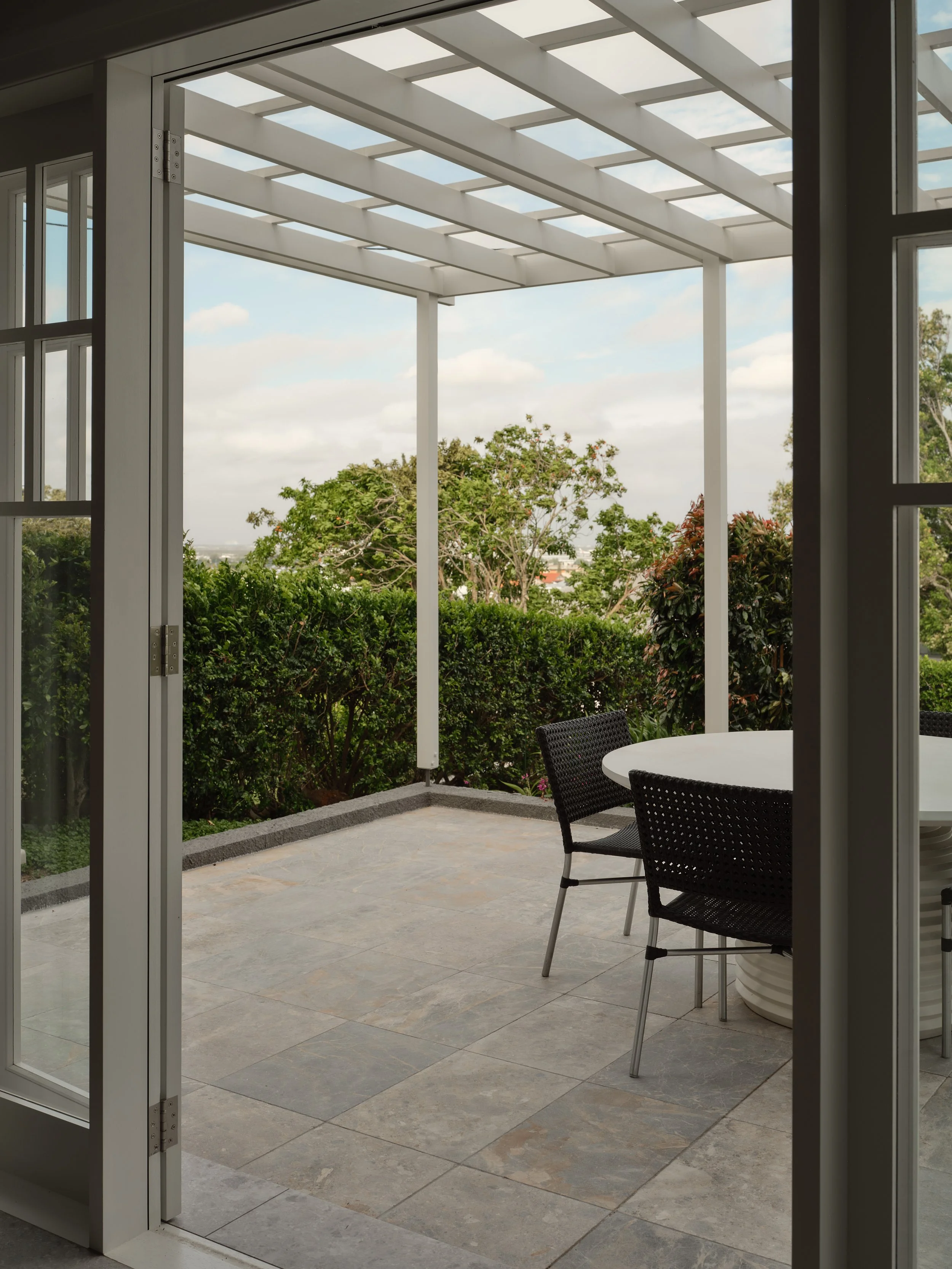 Outdoor dining area under an open pergola with tiled flooring and landscaped garden