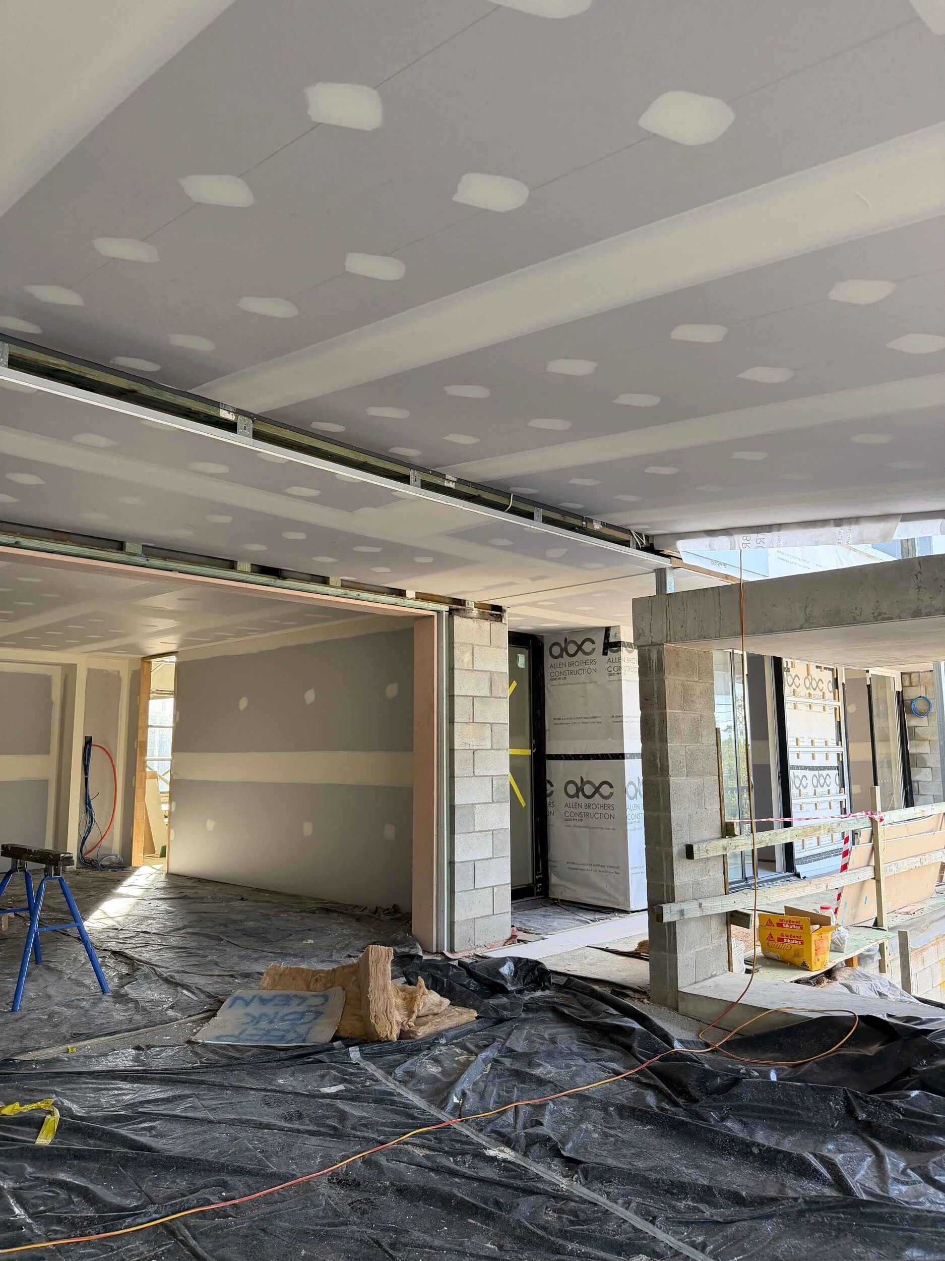 Interior construction progress showing plasterboard installation, concrete block columns and protective floor sheeting during the lock‑up stage of a major architectural renovation by Allen Brothers Construction.