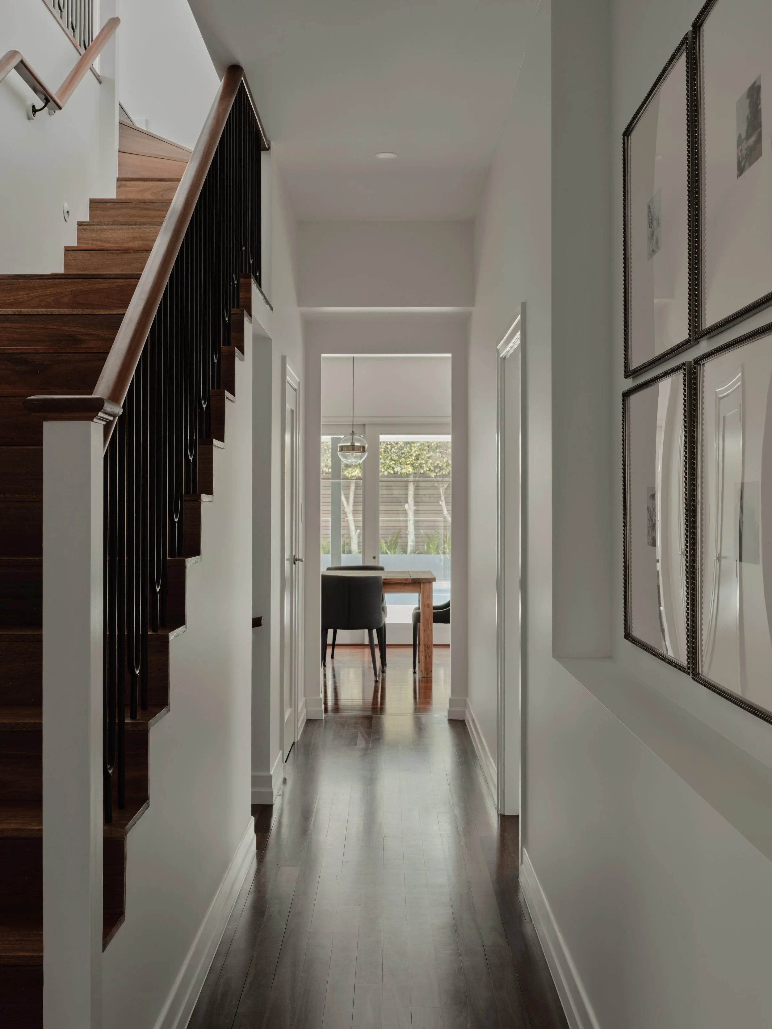 Modern hallway with timber staircase, dark flooring and open‑plan dining area in a renovated heritage home