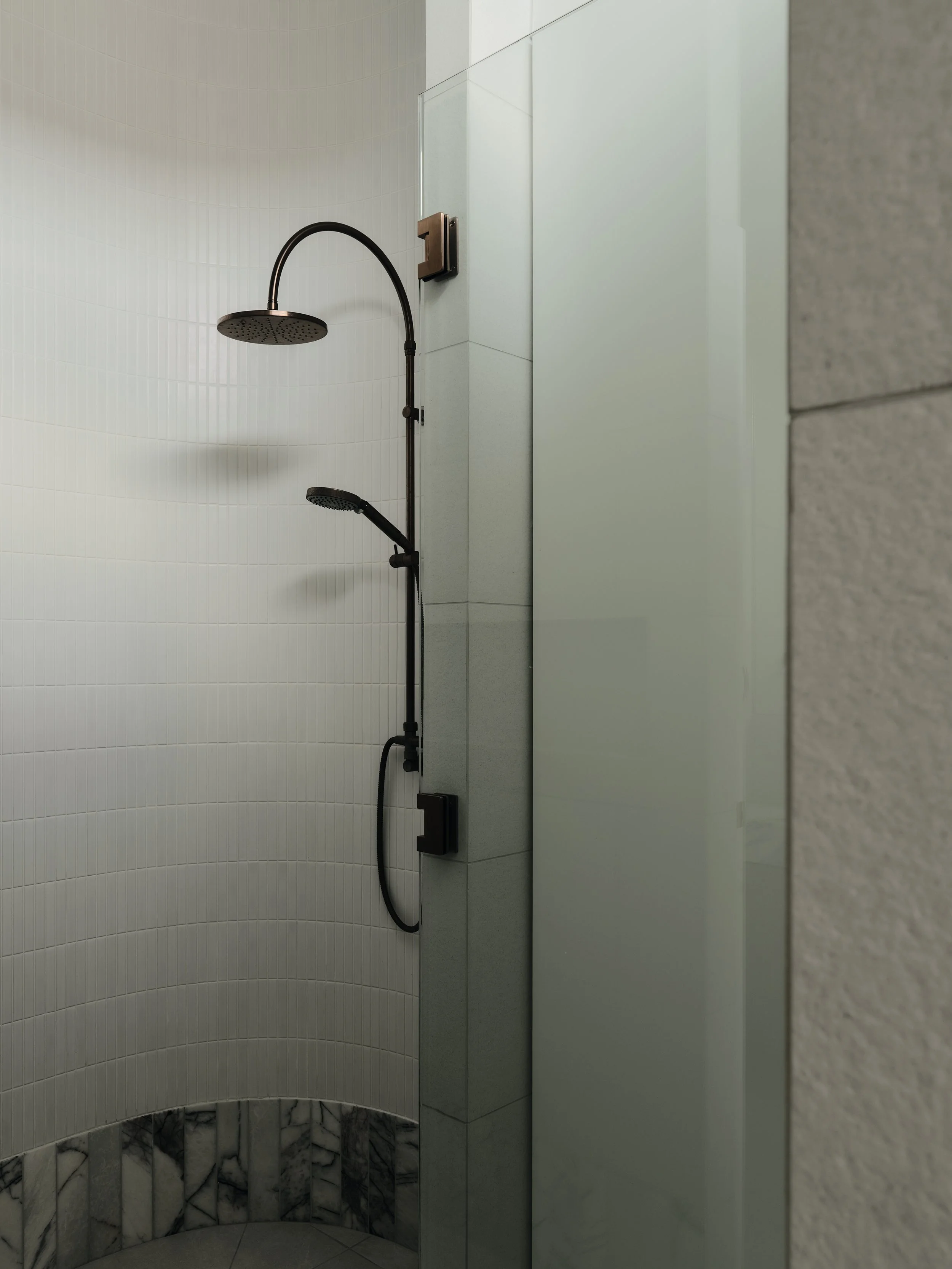 Modern curved‑wall shower with rain head, handheld shower and white vertical tiles in a luxury renovation