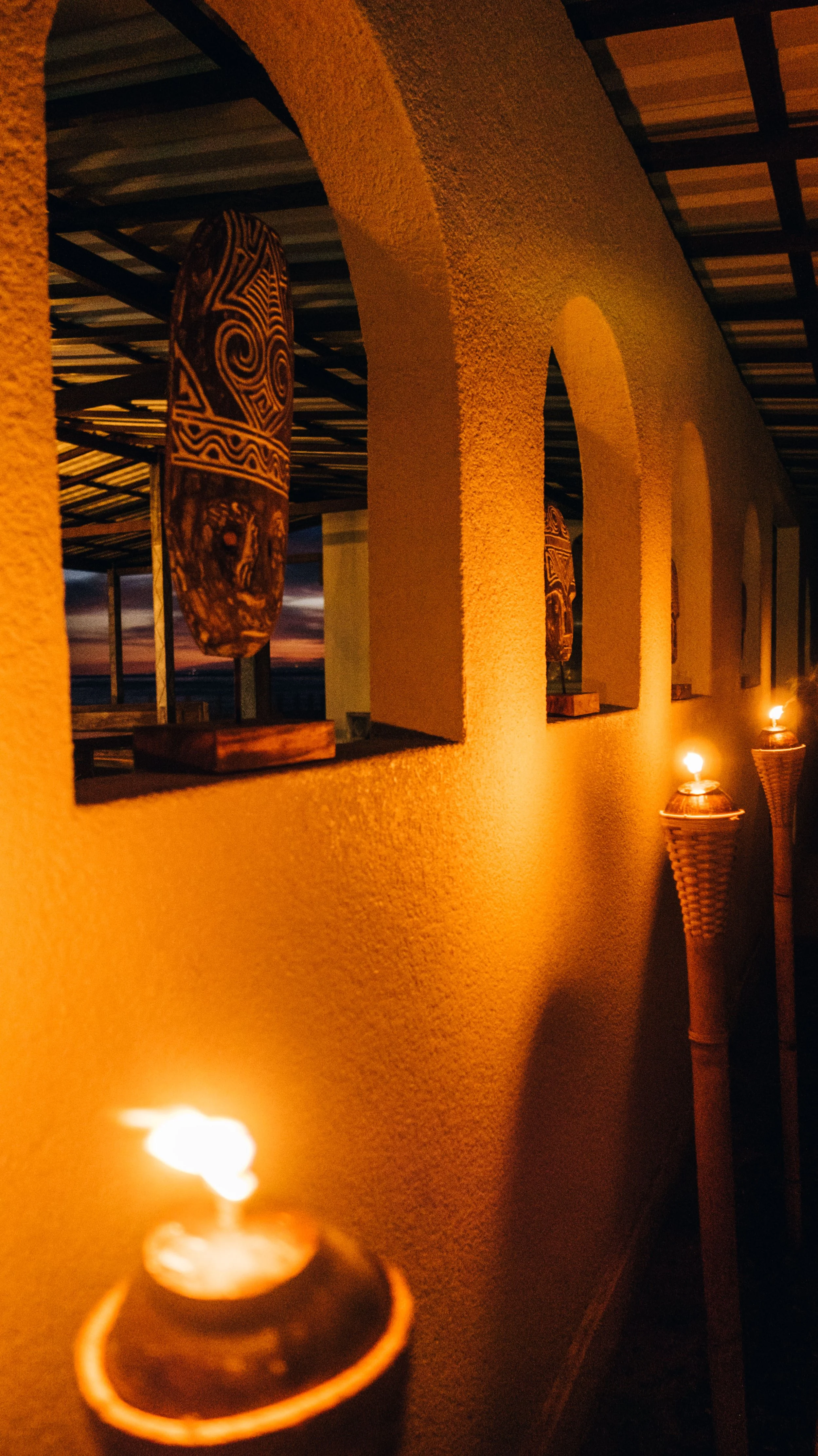 Dimly lit corridor with arched openings, decorated with wall art and tiki torches.