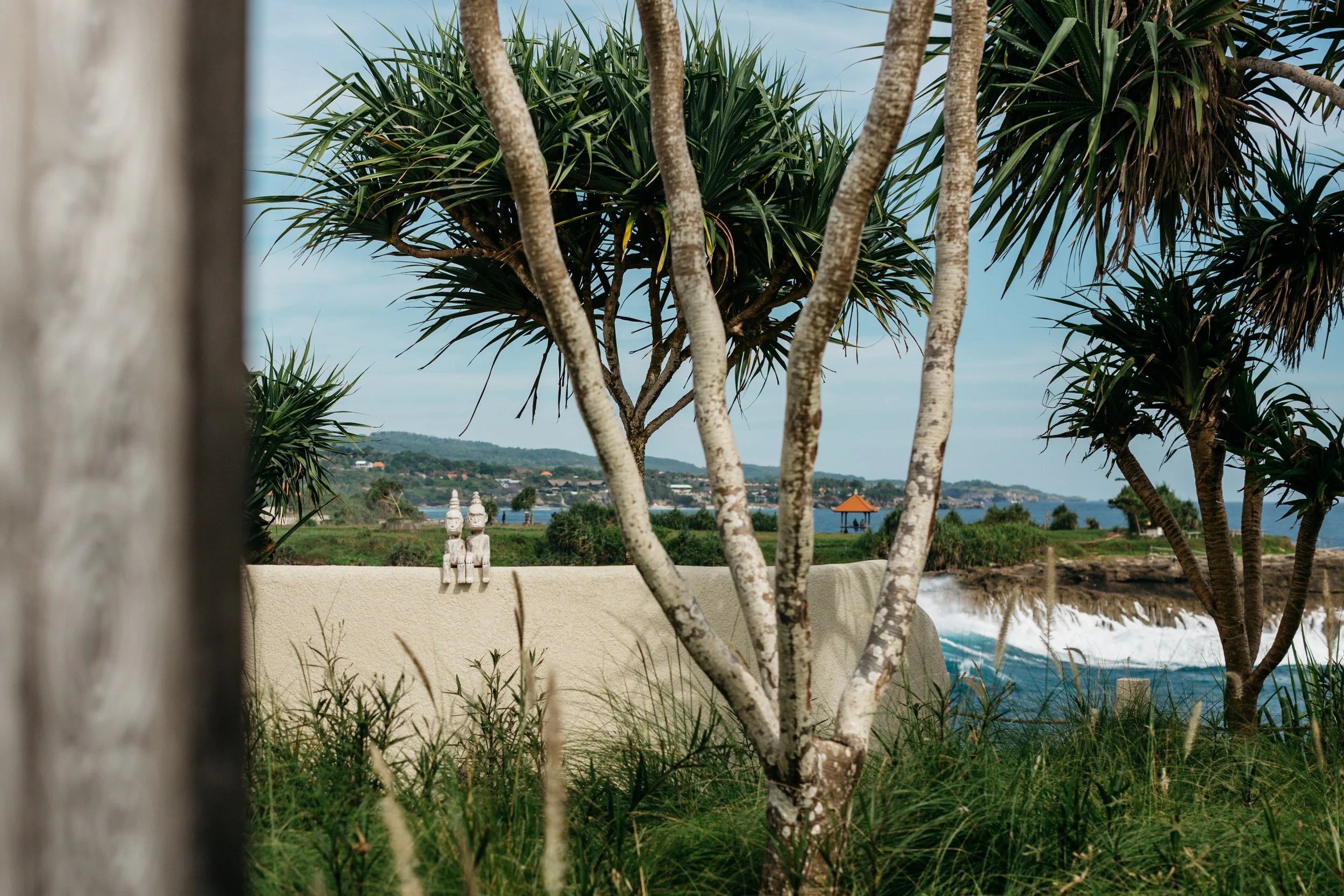 Scenes of a coastal area with trees, a white wall, statues, and the ocean in the background.