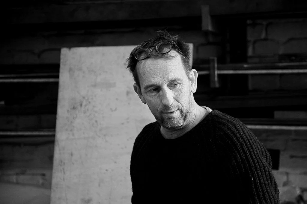 A black and white photo of a man with glasses on his head, wearing a black sweater, looking to the side.