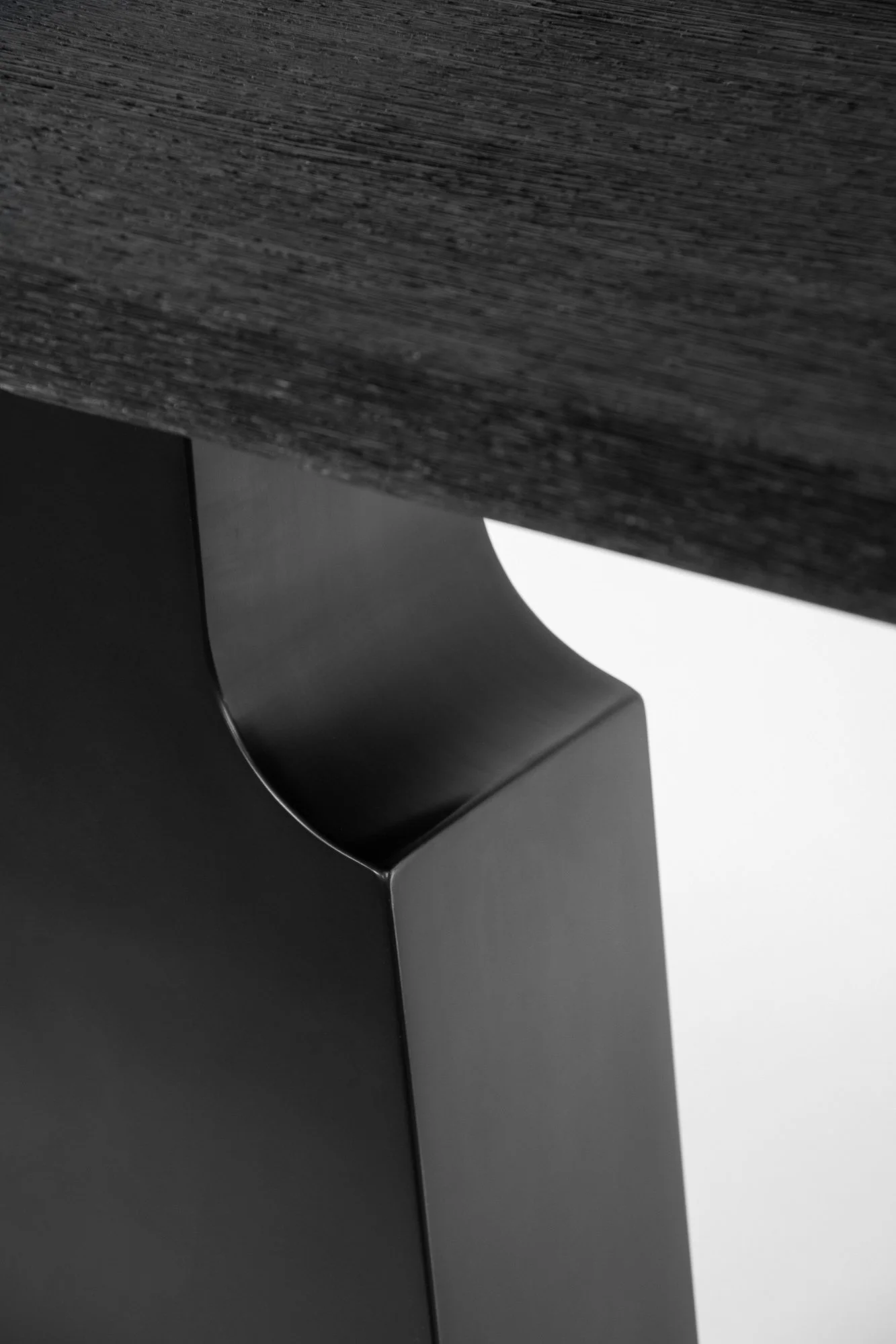 Close-up of a modern, black metal table leg with a curved design, supporting a dark wood tabletop.