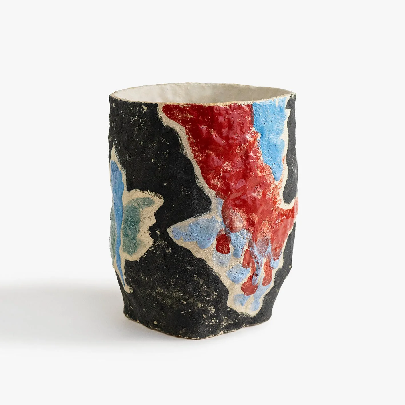 Ceramic cup with abstract painted design in black, red, blue, and beige colors.
