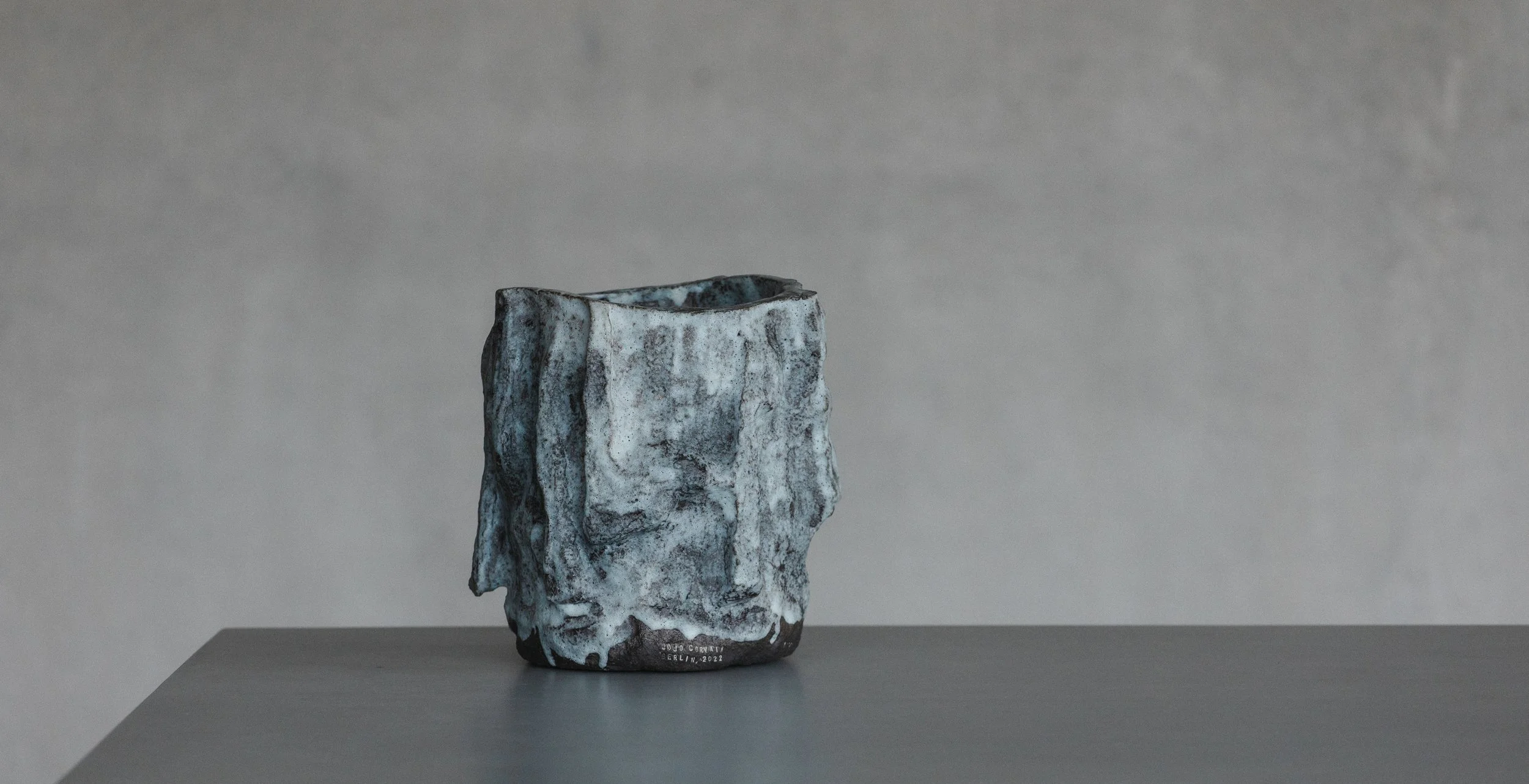A ceramic sculpture resembling a rough, textured rocky face, with a black and white marbled glaze, set on a plain gray surface with a gray background.
