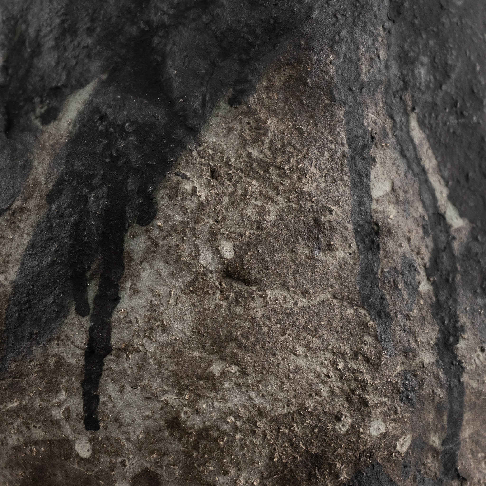 Close-up of a ceramic surface with dark and light patches, cracks, and rough textures.