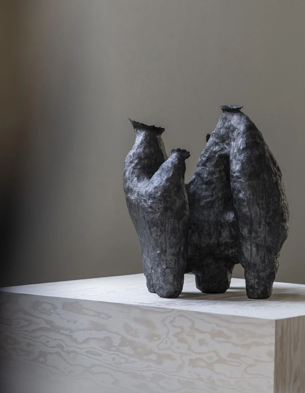 A black ceramic sculpture of three abstract, organic shapes resembling animals or natural forms on a light wooden surface against a plain wall.