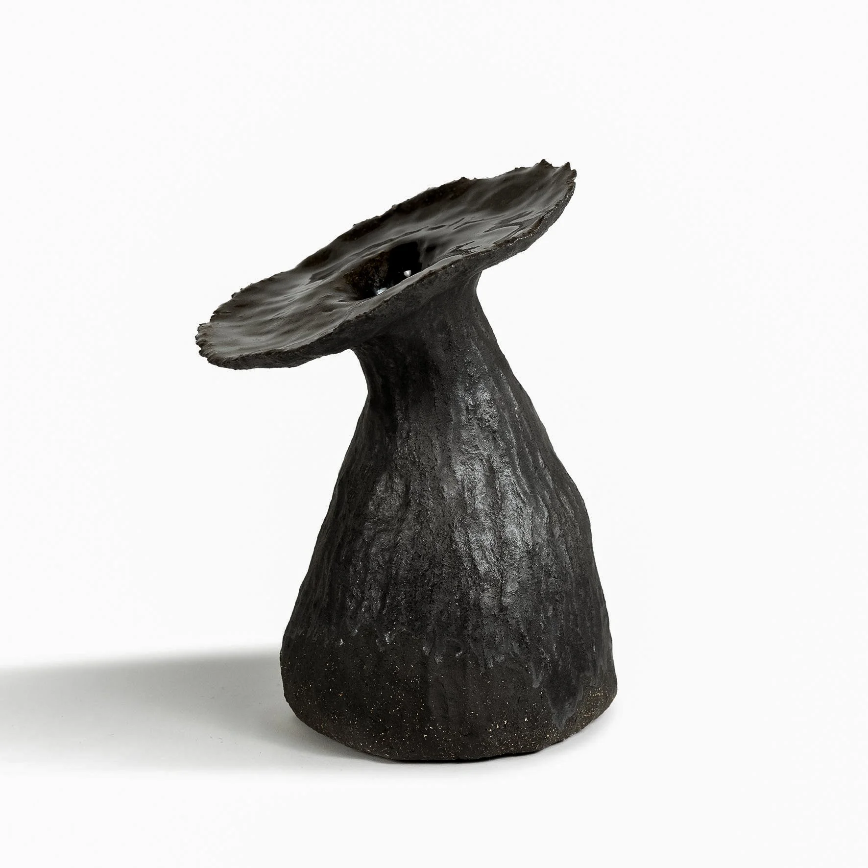 Black textured ceramic sculpture resembling a mushroom with a wide, flat cap and a narrow stem, set against a white background.