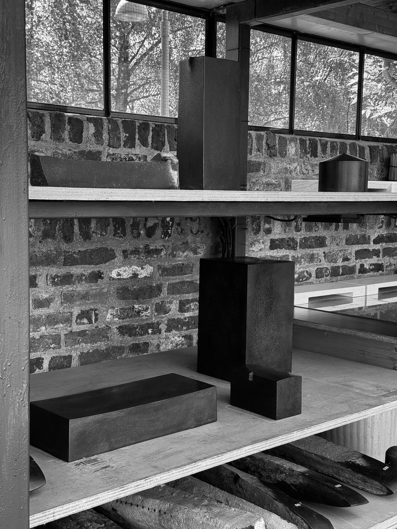 Black and white photo of modern decorative objects on wooden shelves against a brick wall, with a window showing trees outside.