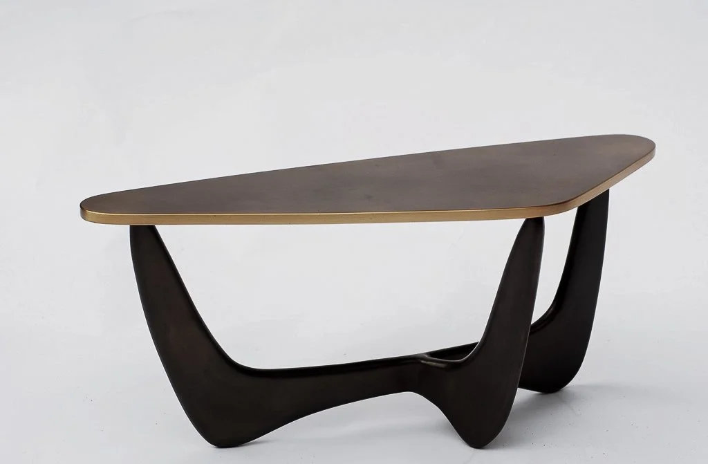 Modern coffee table with a dark, curved wooden base and a flat, irregularly shaped brass top.