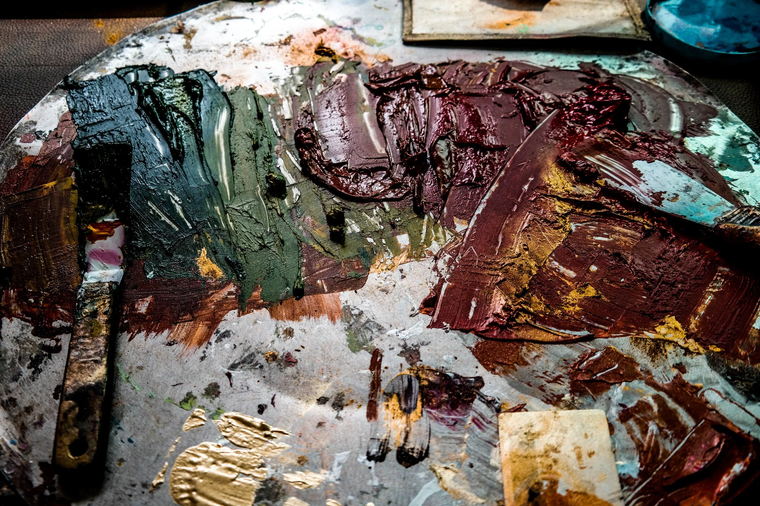 Mixed oil paints on a painter's palette with a palette knife and paint smudges.