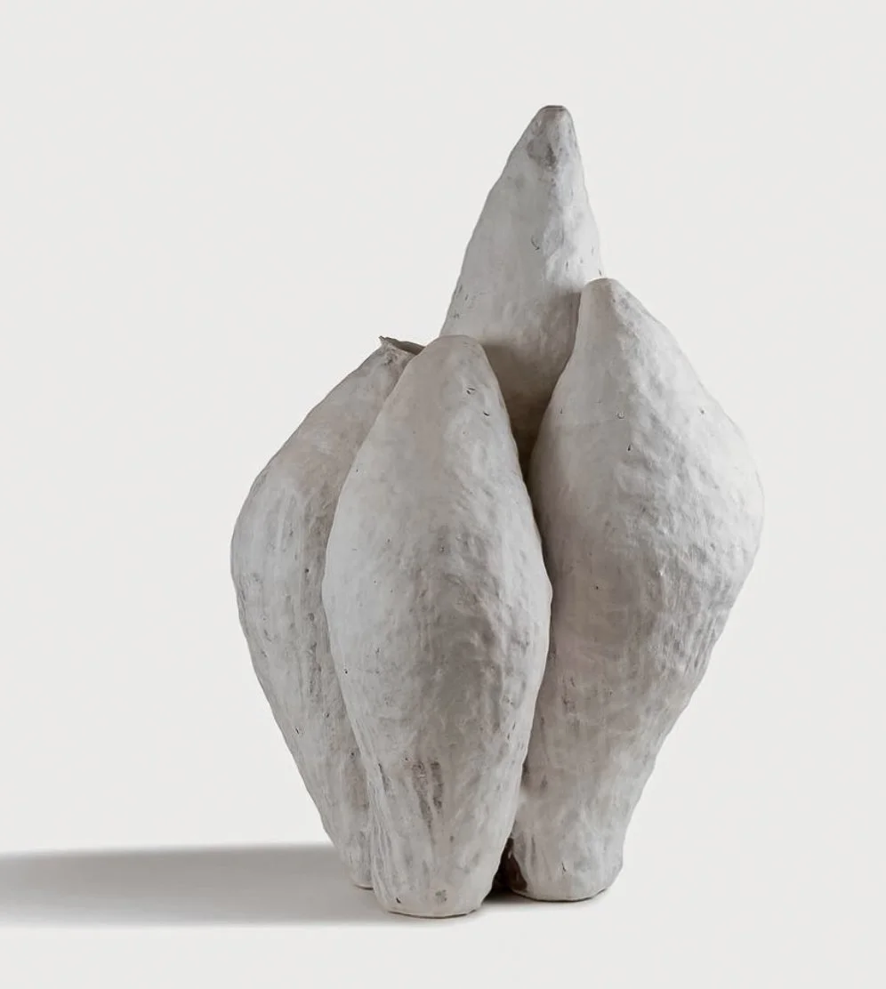 White ceramic sculpture resembling a cluster of elongated stones or shells on a plain white background.