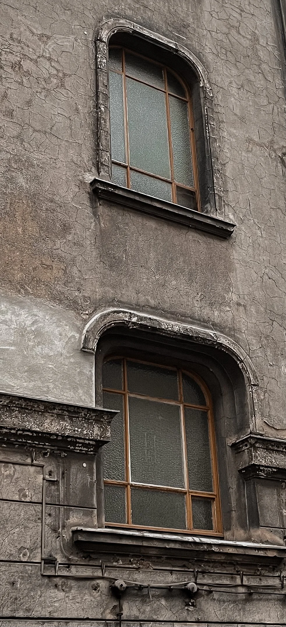 Two old, weathered windows with wooden frames set in a cracked and aged gray stone wall.