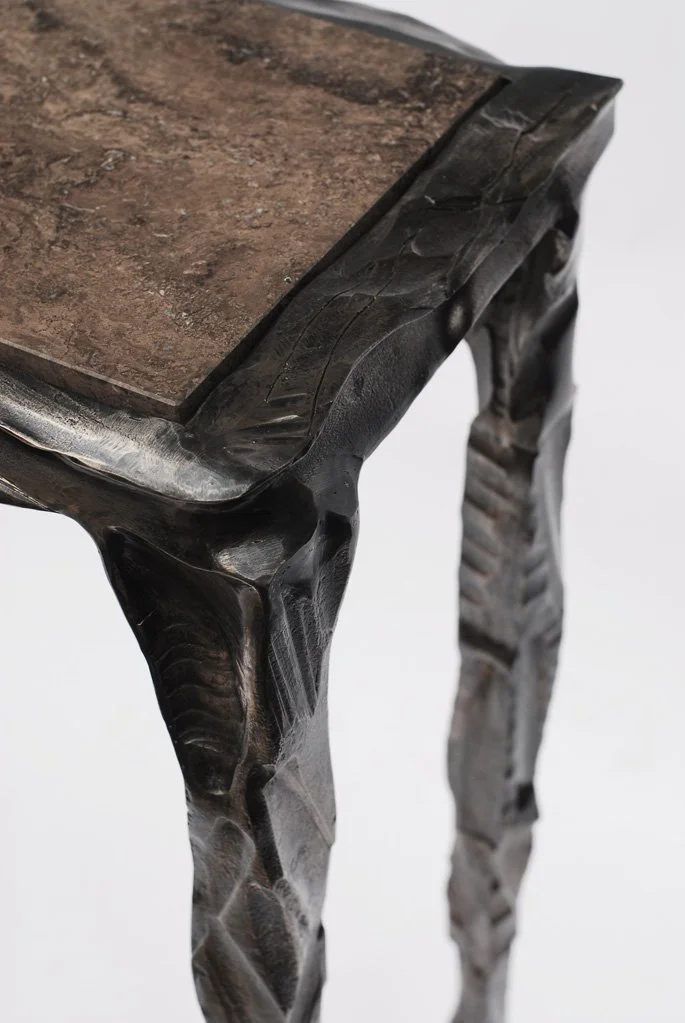 Close-up of a handcrafted steel console  with a dark polished finish, featuring a textured and carved edge design.