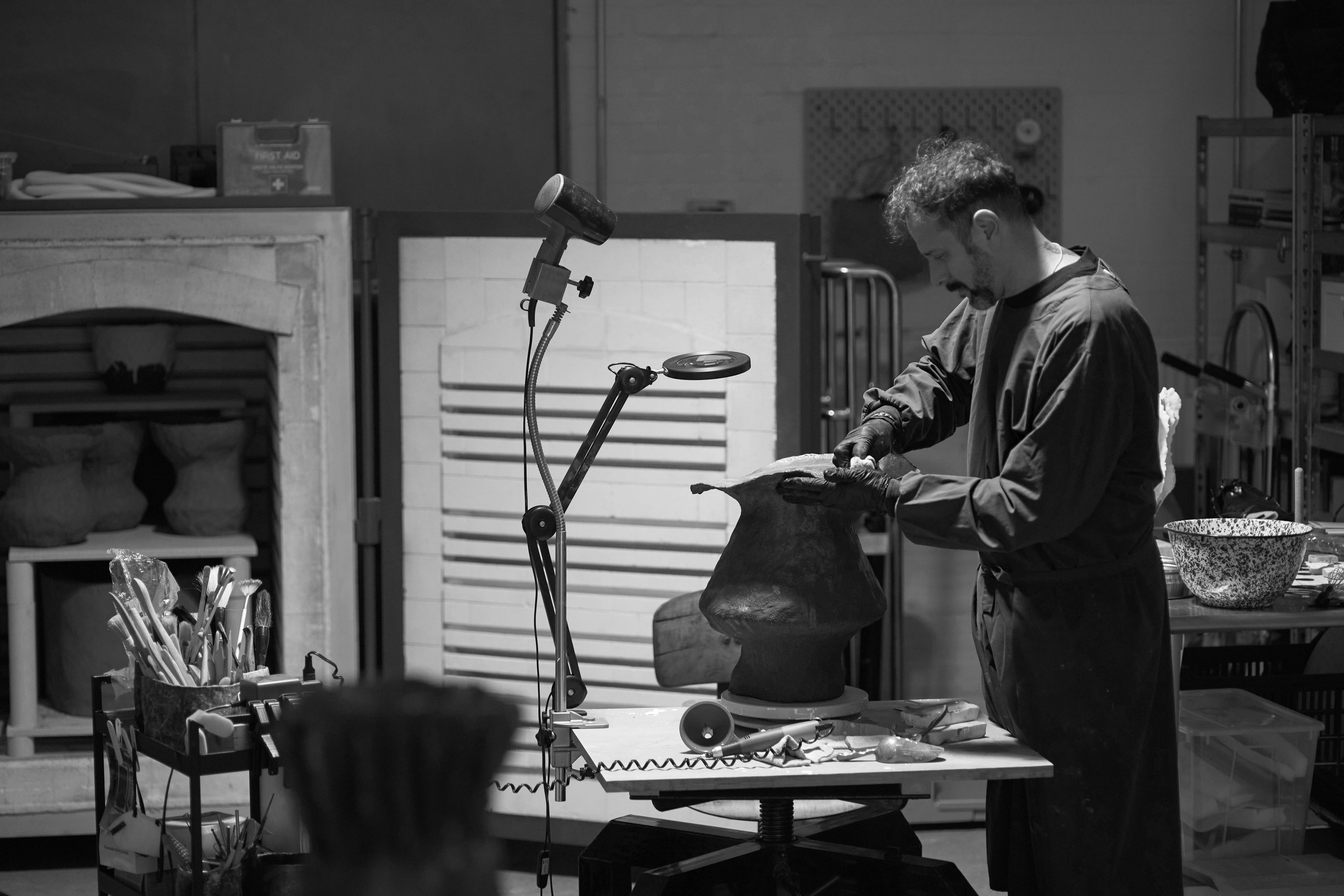A person working on an art sculpture in a studio, surrounded by art tools, shelves, and art supplies.