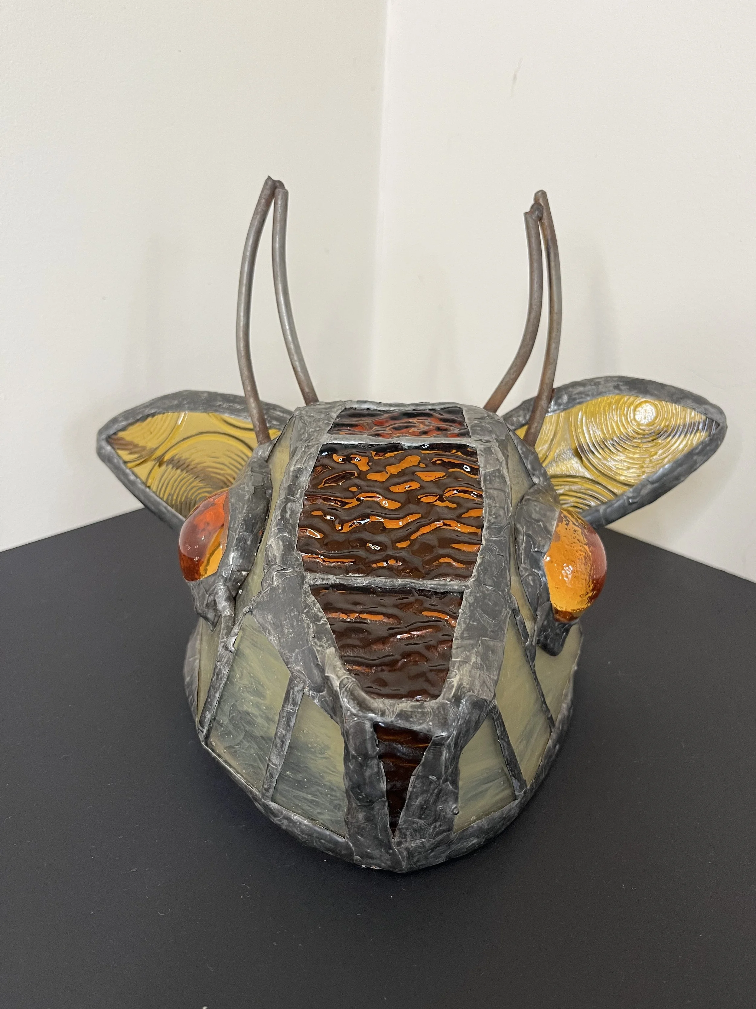 “Amber” (2026), Glass, welded steel, solder, 26(w) x 16(h) x15(d) cm. Glasswork by Kirsten Laken of Spirit of Glass.