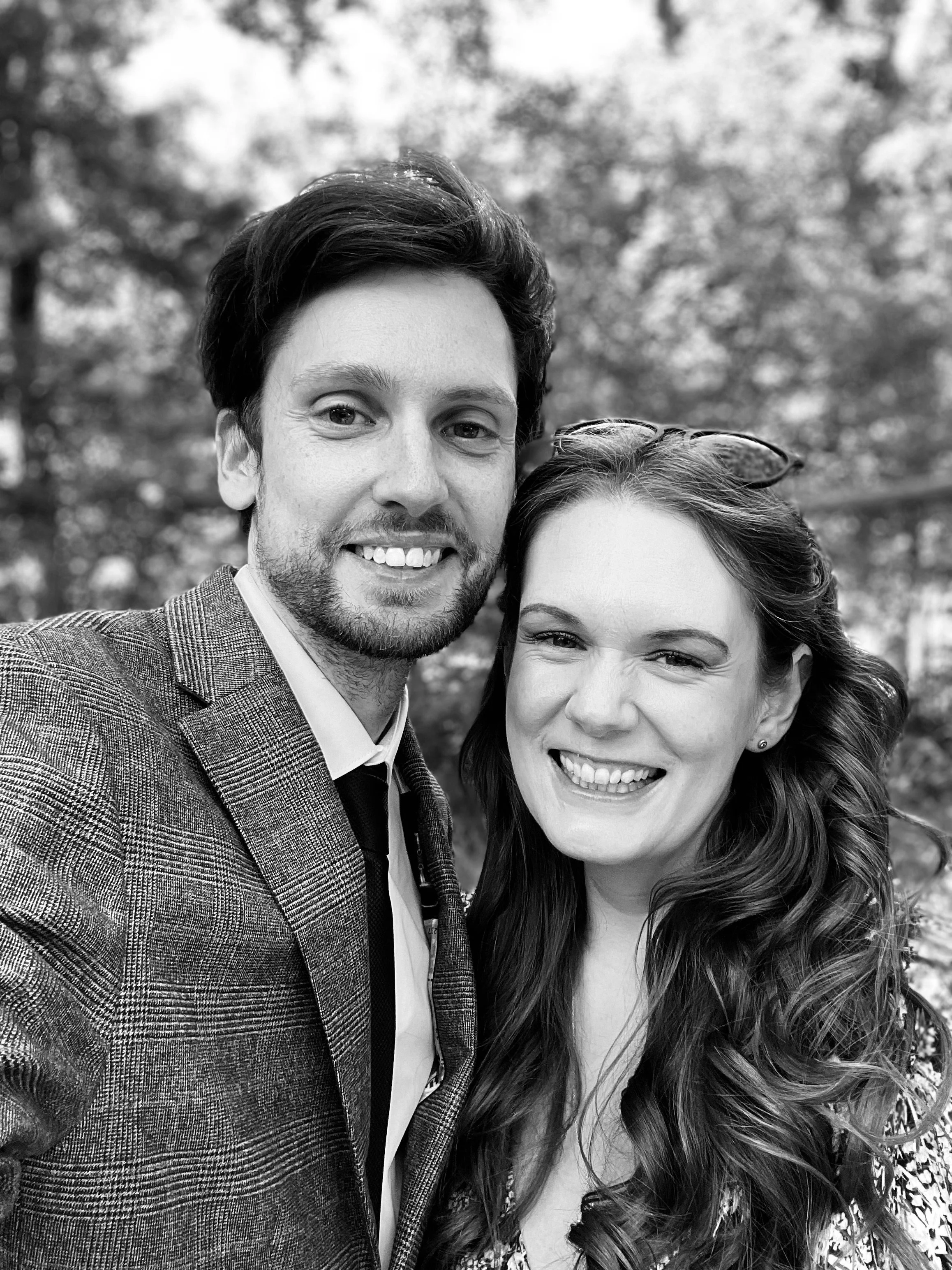 Black and white photo of a smiling man and woman outdoors, close-up selfie, nature background.