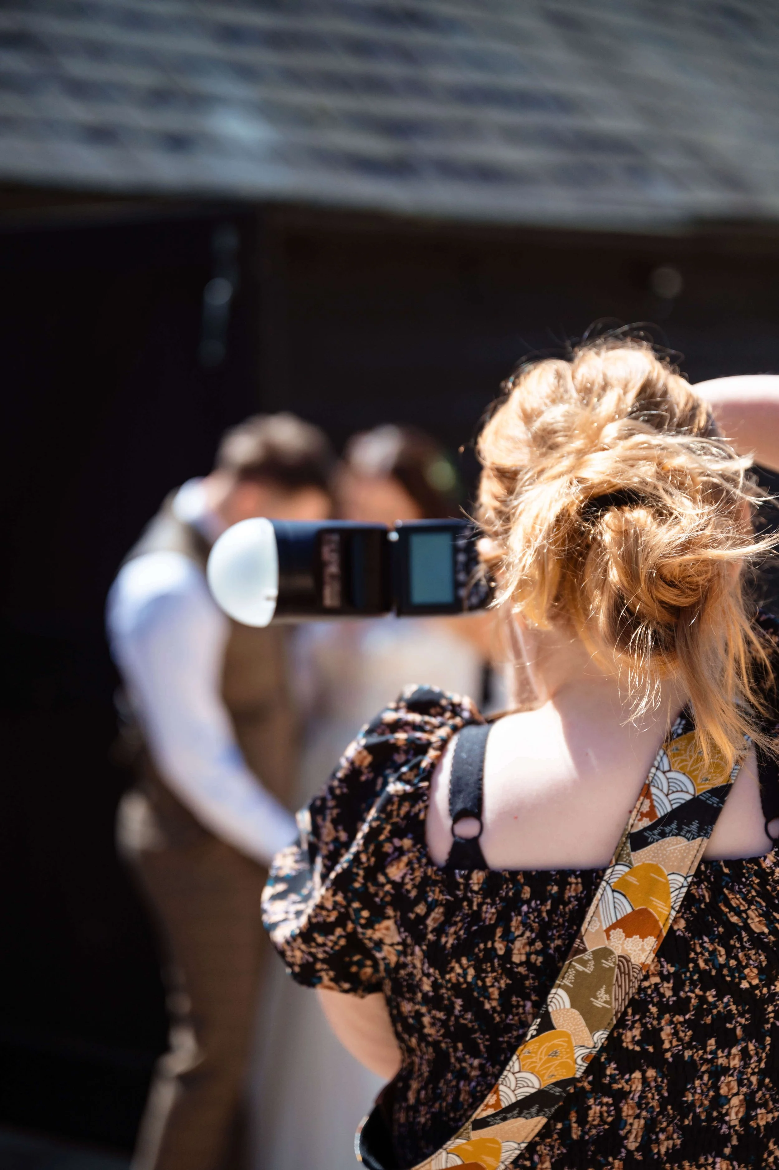 A woman taking a photo with a camera of a bride and groom in wedding attire.