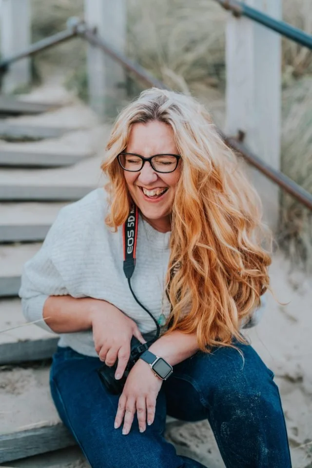 Woman with long red hair and glasses sitting on outdoor stairs, laughing