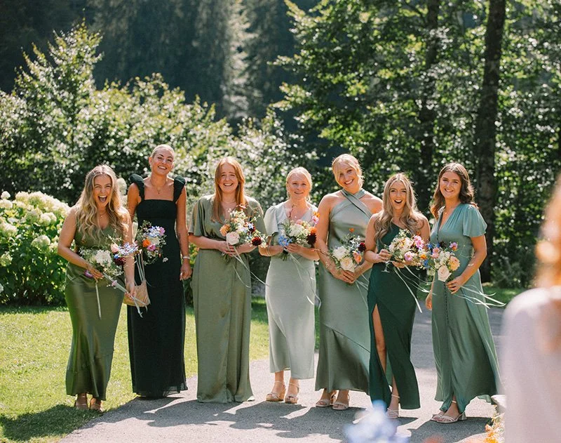 Group of bridesmaids in beautiful shades of green dresses, holding colourful floral bouquets at Lake Montriond border
