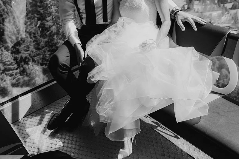 Black and white photo of a bride in a wedding gown sitting with a groom in a suit in a Morzine gondola. border