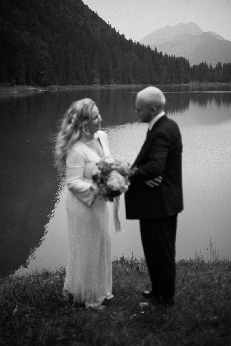 Balck and white image of a bridge and groom smiling at each other, in front of Lake Montriondborder